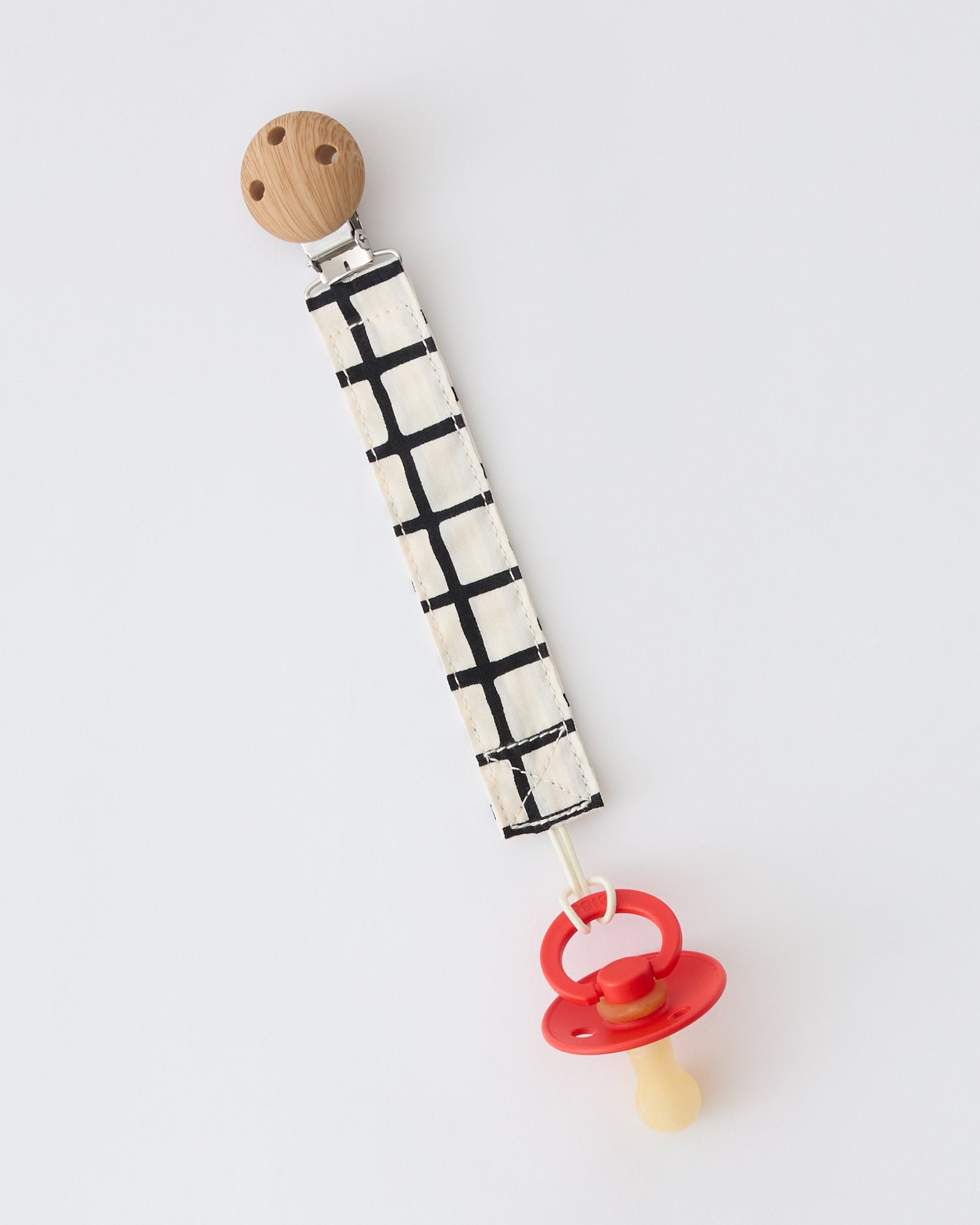 Pacifier Clip Two-Pack in Black Grid with pacifier attached, on a beige background.