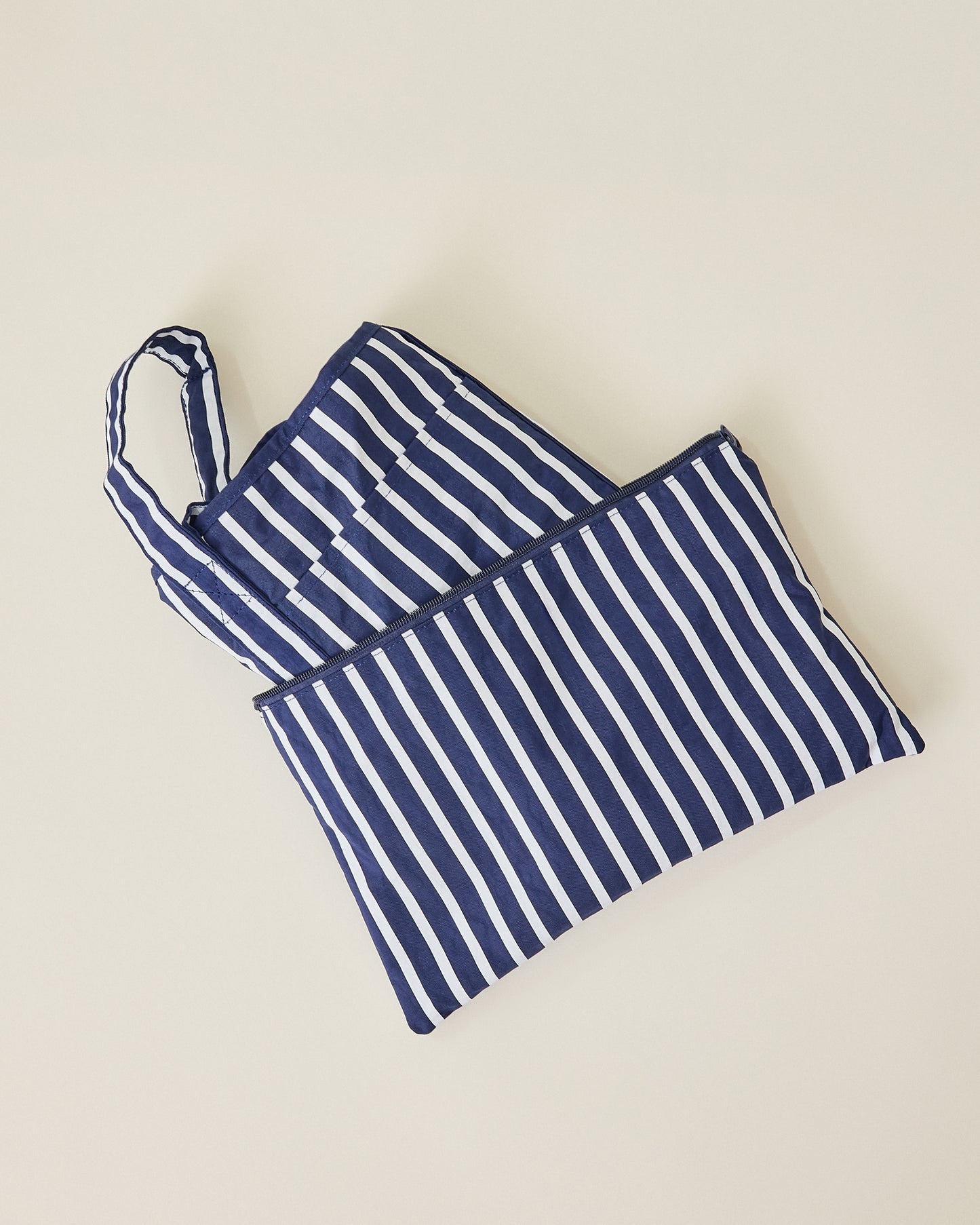Navy blue and white striped Packable Park Carryall folded up with included matching pouch on a beige background