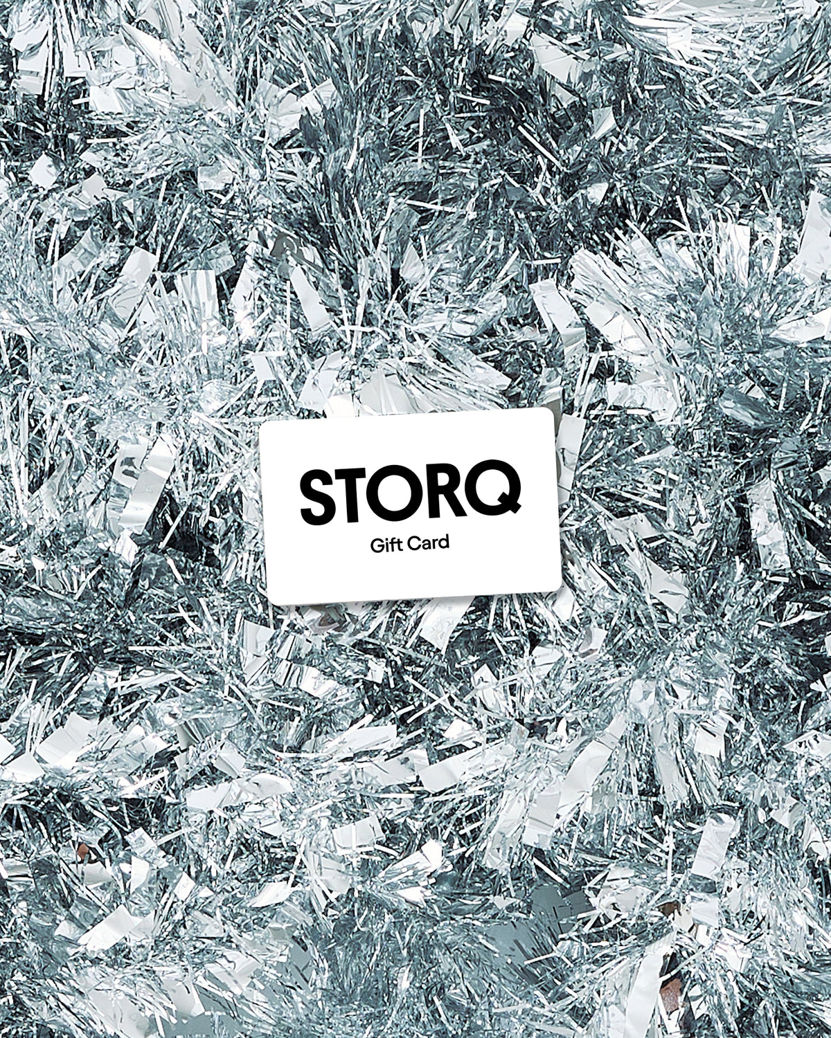 A white rectangular gift card with the text 'STORQ Gift Card' in black, placed on top of bright and shiny silver tinsel decoration.