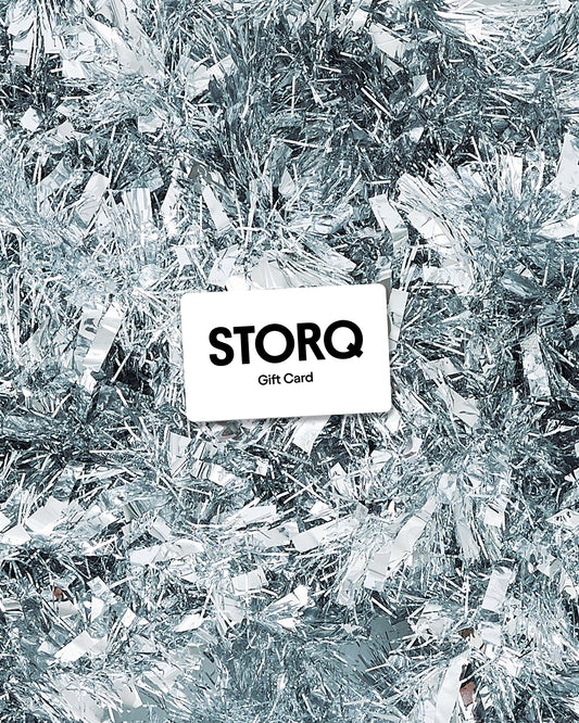 A white rectangular gift card with the text 'STORQ Gift Card' in black, placed on top of bright and shiny silver tinsel decoration.