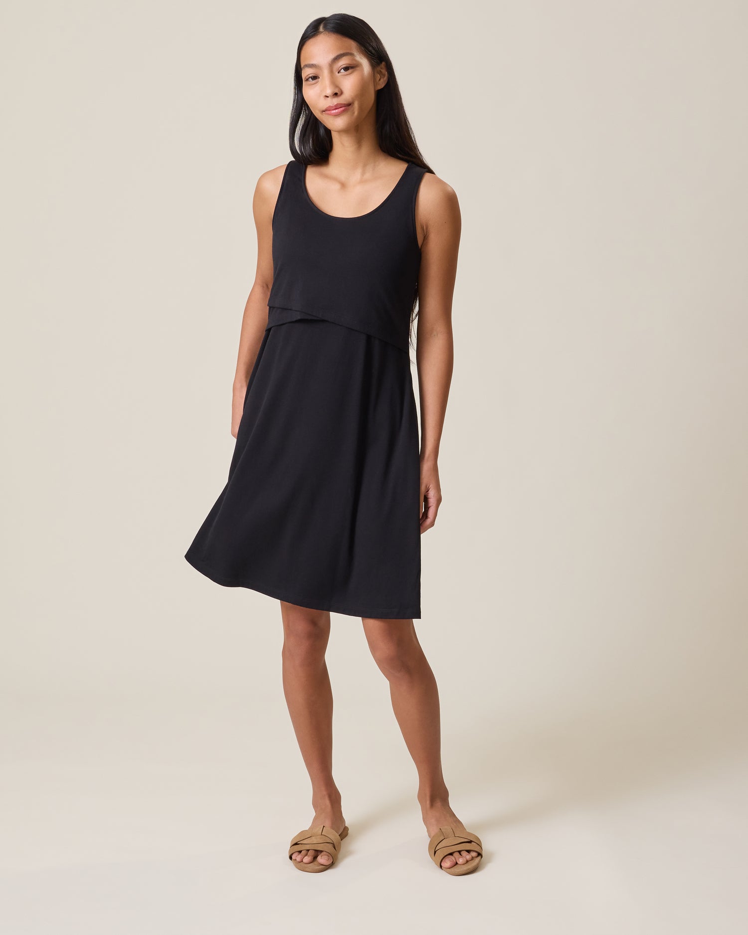 Woman wearing a black sleeveless Penelope Nursing dress on a beige background@model_info:Charissa is 5'7" and wearing a Small.