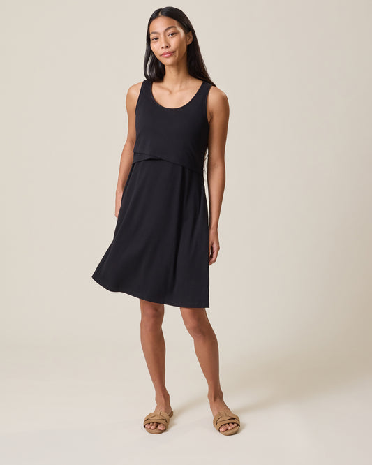 Woman wearing a black sleeveless Penelope Nursing dress on a beige background@model_info:Charissa is 5'7" and wearing a Small.