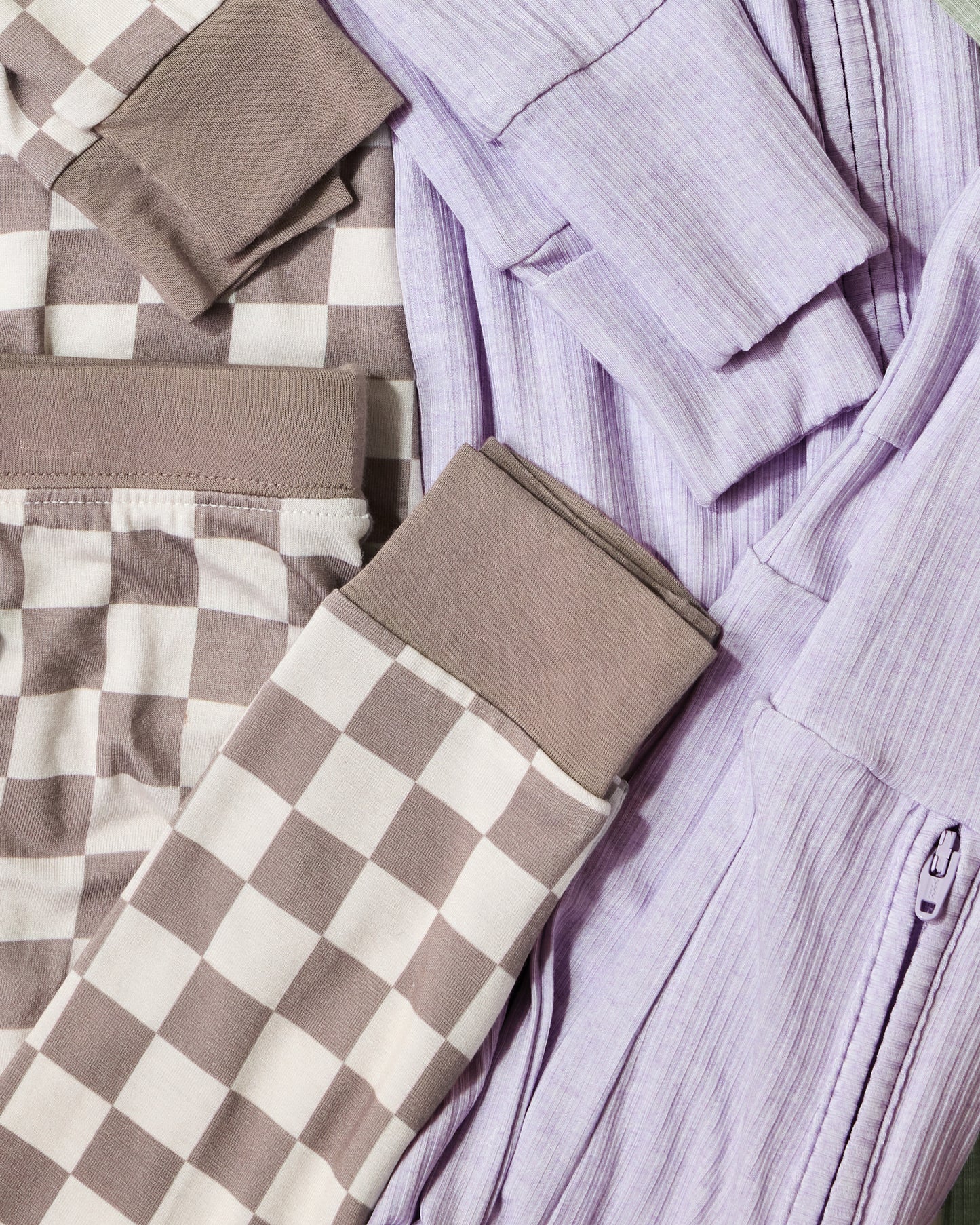 Folded baby pajamas on a flat surface, one checkered and one ribbed