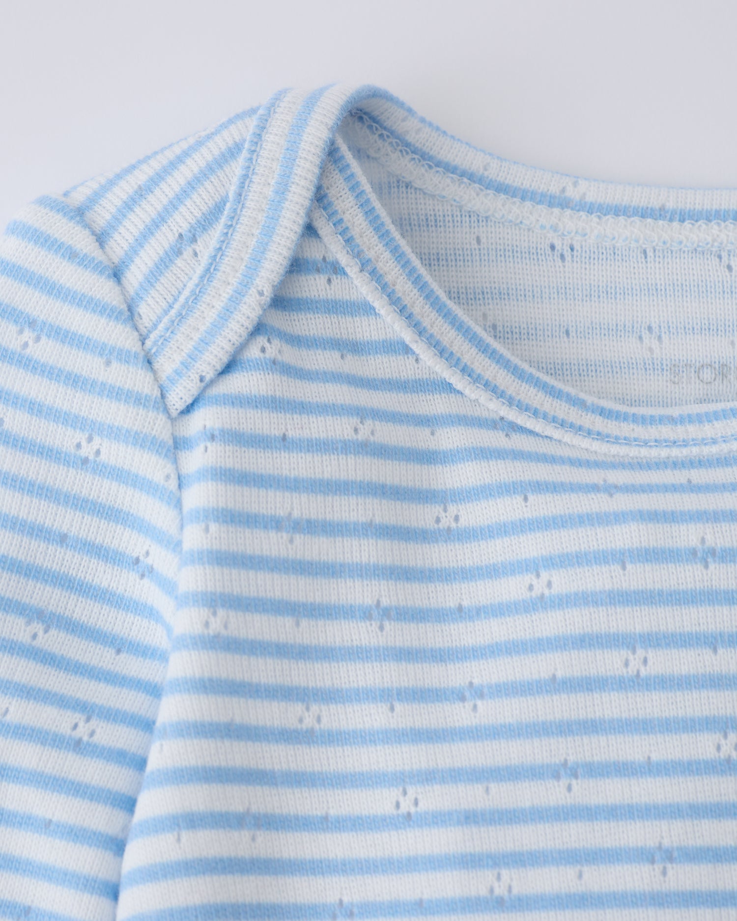 Close up of collar detail on the Pointelle Long Sleeve Onesie in Blue Candy Stripe on a beige background.