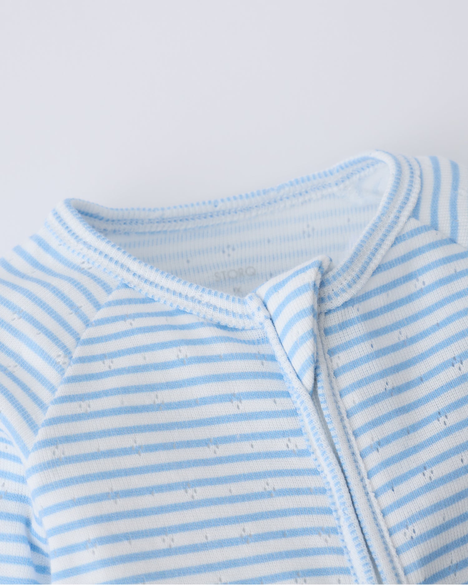Close up of collar and zipper detail on the Pointelle Sleeper Pajama in Blue Candy Stripe on a beige background.