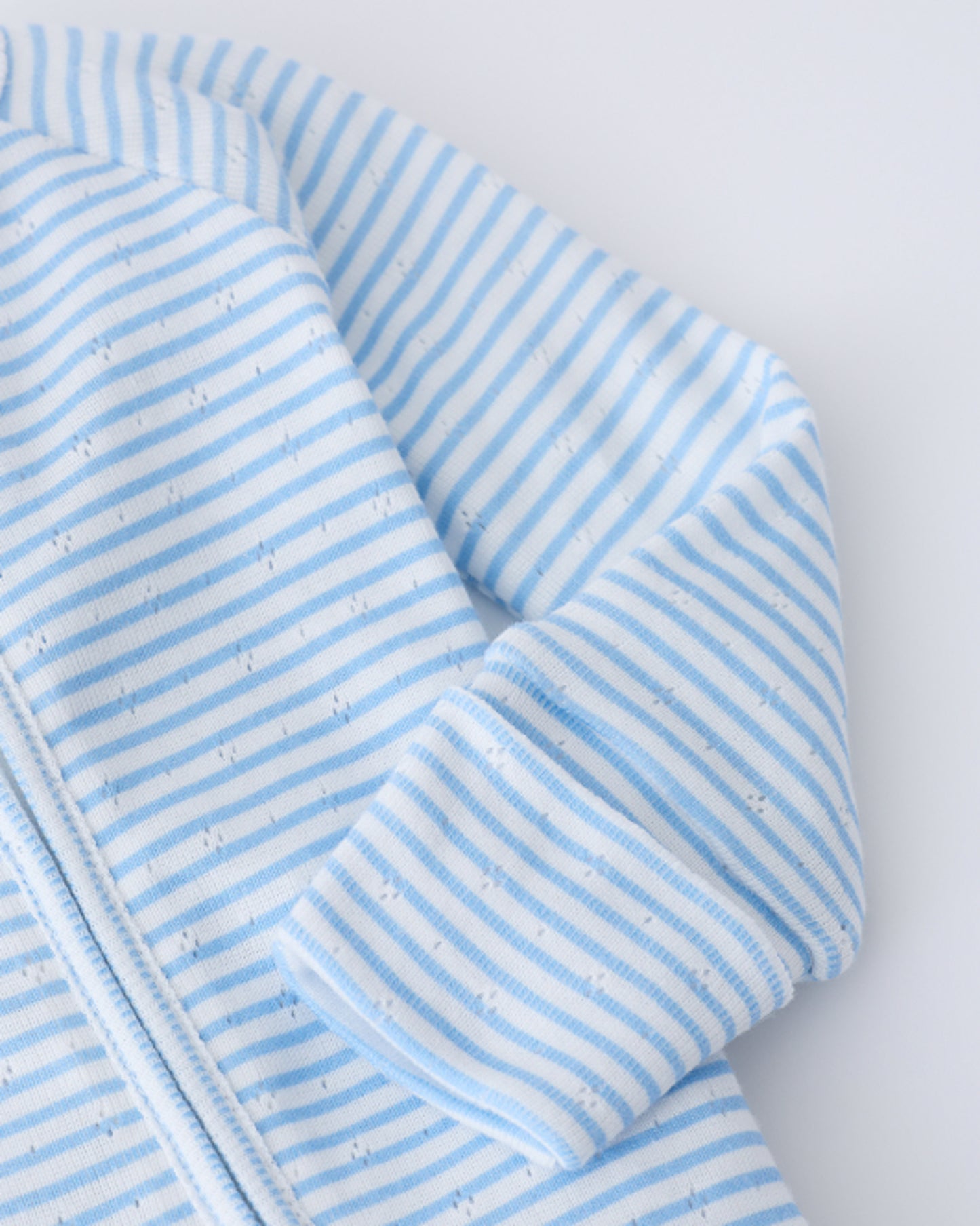 Close up of sleeve detail on the Pointelle Sleeper Pajama in Blue Candy Stripe on a beige background.