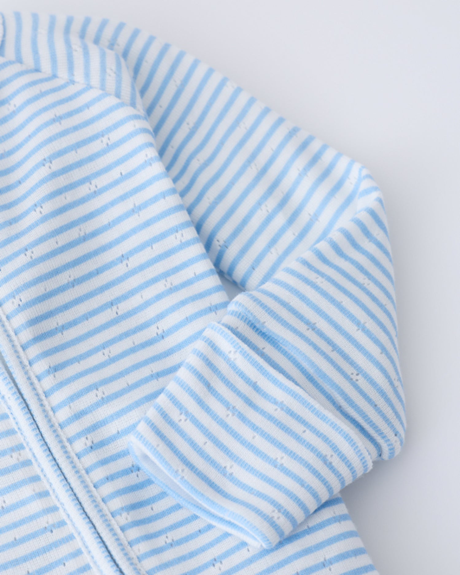 Close up of sleeve detail on the Pointelle Sleeper Pajama in Blue Candy Stripe on a beige background.