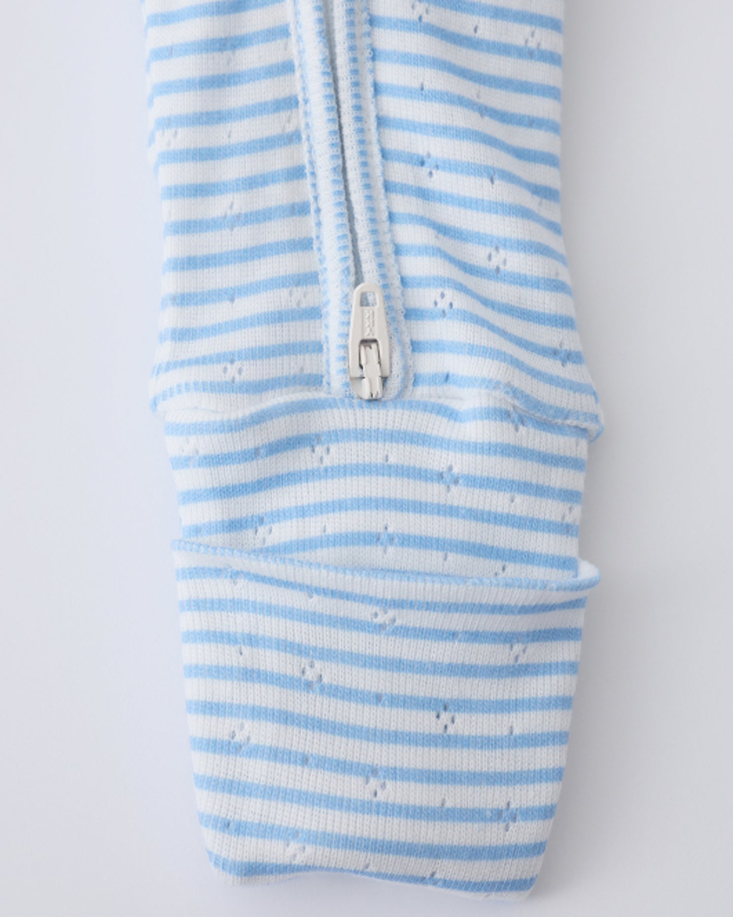 Close up of the pant leg zipper detail on the Pointelle Sleeper Pajama in Blue Candy Stripe on a beige background.