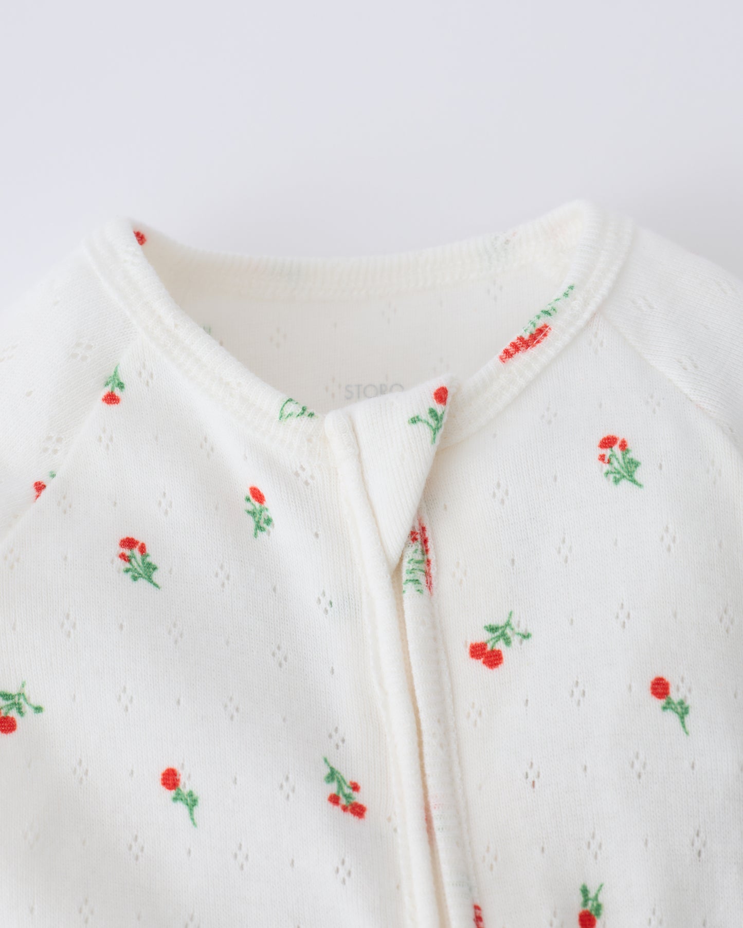 Close up of collar and zipper of the Pointelle Sleeper Pajama in Dainty Ditsy on a beige background.
