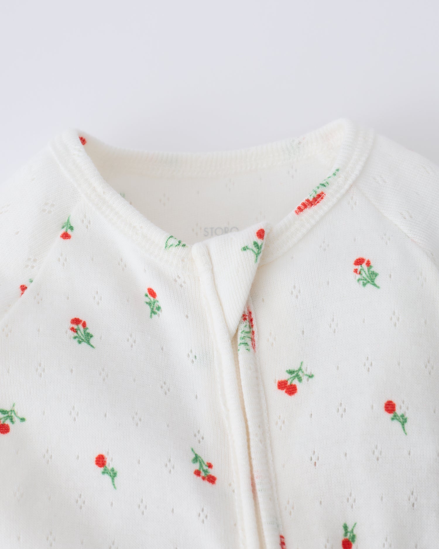 Close up of collar and zipper of the Pointelle Sleeper Pajama in Dainty Ditsy on a beige background.