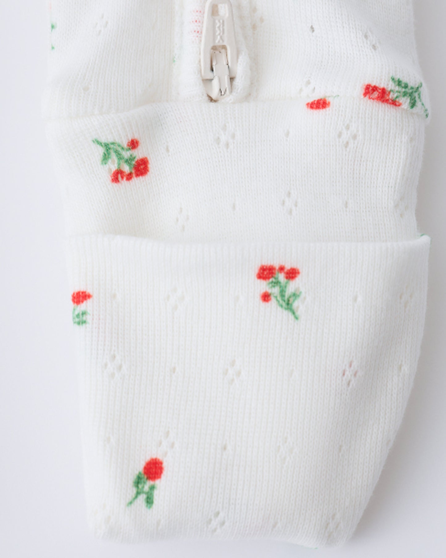 Close up of pant leg zipper on the Pointelle Sleeper Pajama in Dainty Ditsy on a beige background.