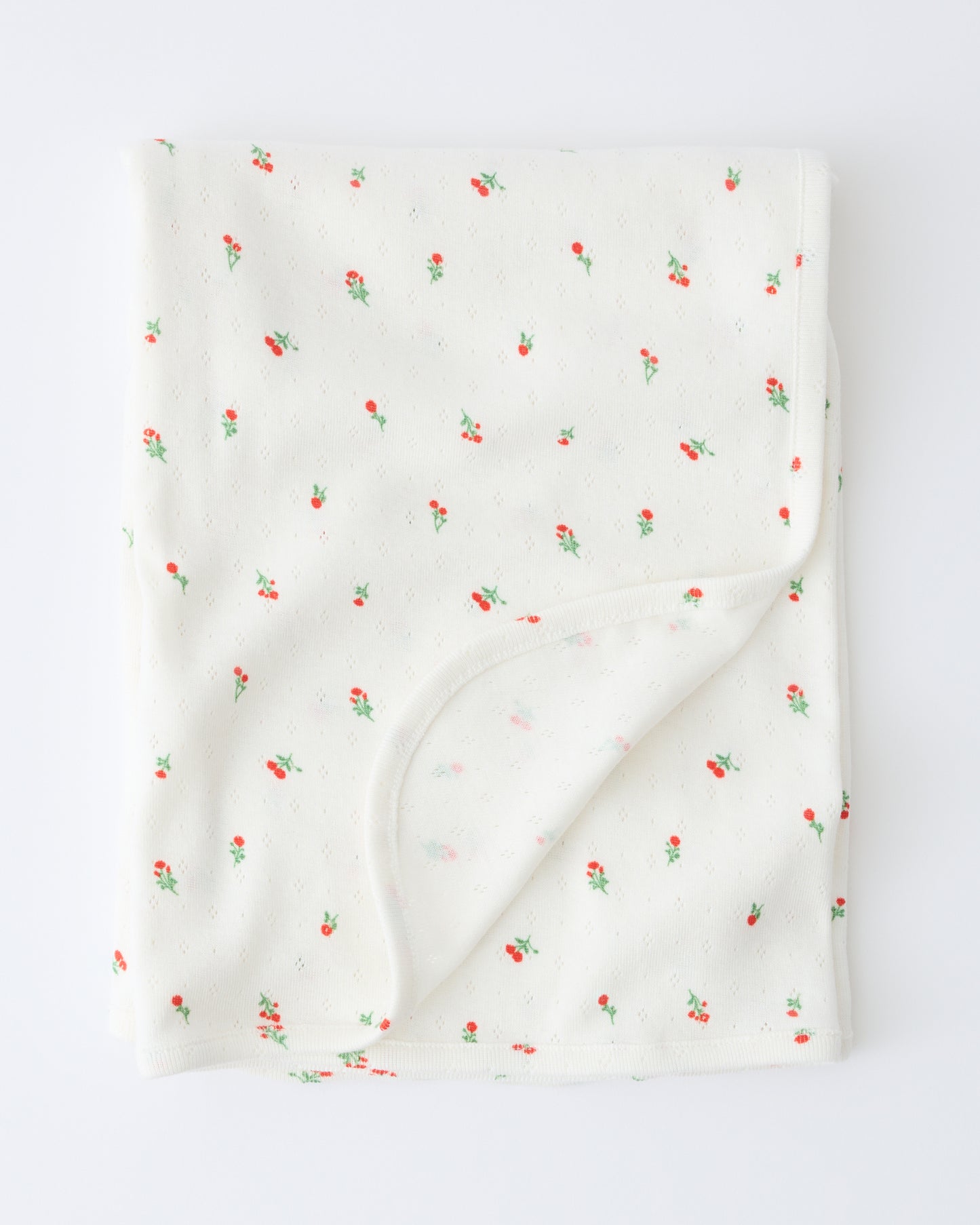 Pointelle Swaddle in Dainty Ditsy pattern folded with a flipped corner to show reverse side, on a beige background.