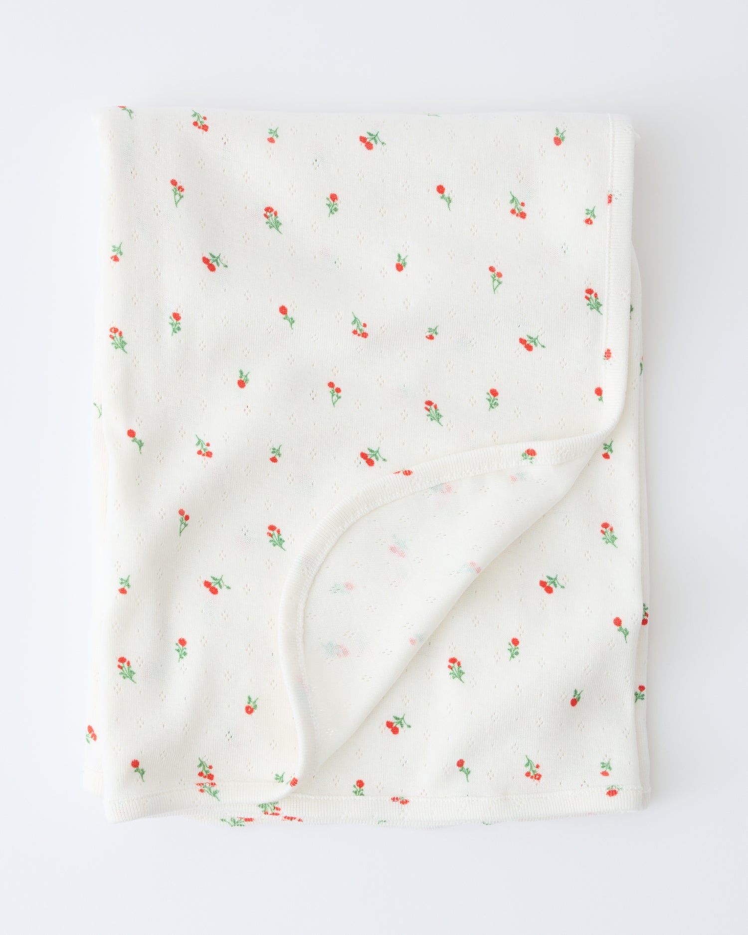 Pointelle Swaddle in Dainty Ditsy pattern folded with a flipped corner to show reverse side, on a beige background.