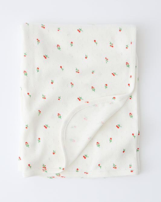Pointelle Swaddle in Dainty Ditsy pattern folded with a flipped corner to show reverse side, on a beige background.