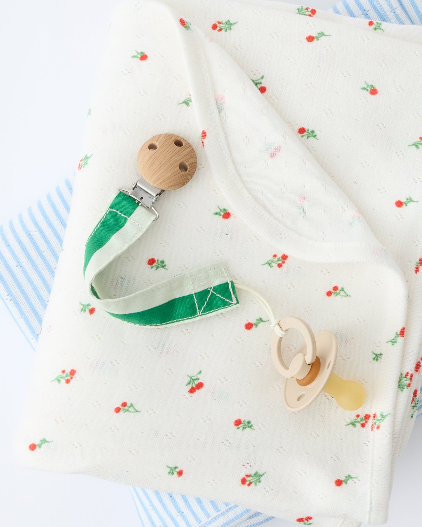 Pacifier Clip Two-Pack in Teal Gingham placed on soft blankets, on a beige background.