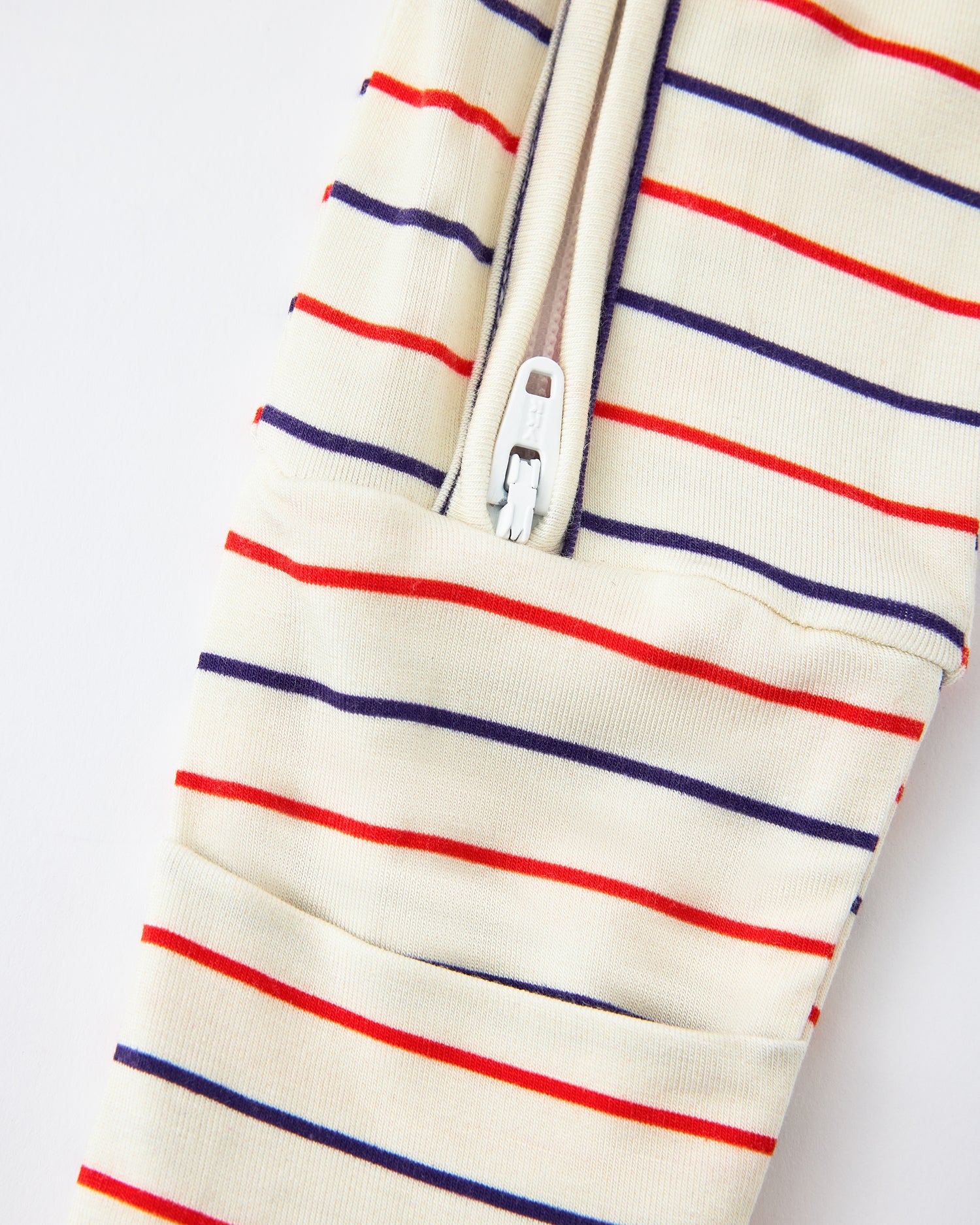 Close up of zipper detail on Bamboo Baby Pajama in Pencil Stripe on a beige background