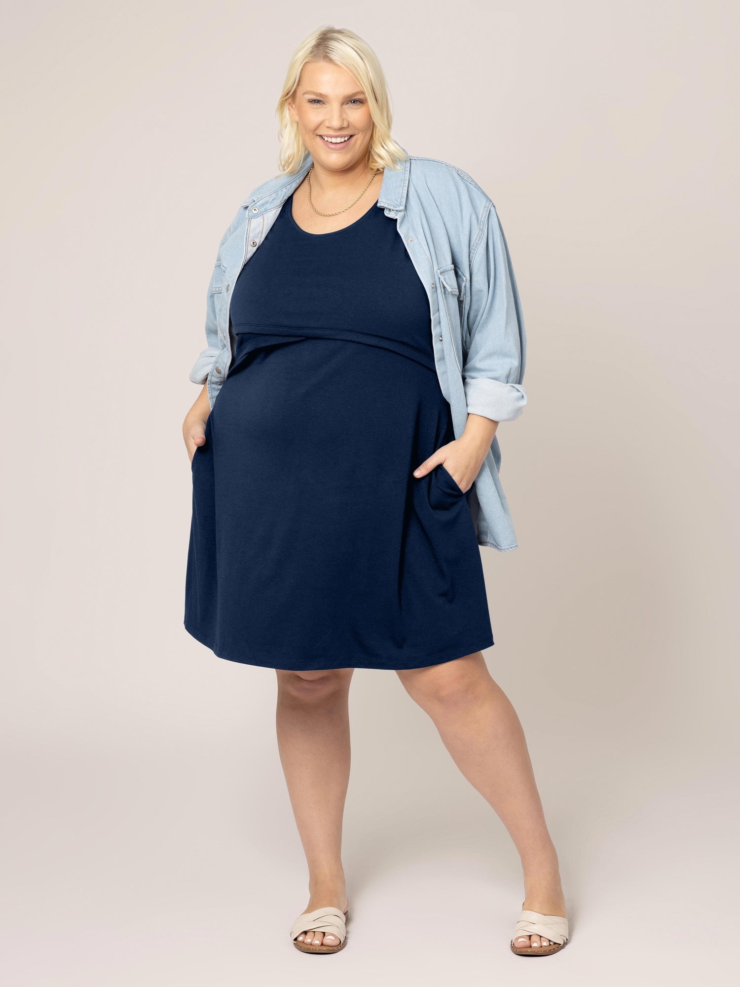 Full image of model wearing the Penelope Crossover Nursing Dress in navy, with hands in pockets, paired with denim jacket and sandals