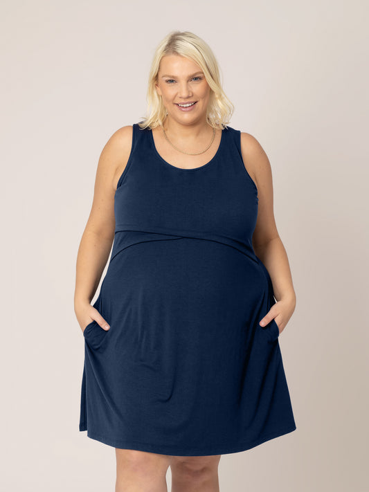 Front view of model wearing the Penelope Crossover Nursing Dress in navy, with hands in pockets. @model_info:Lauren is wearing a 1X.