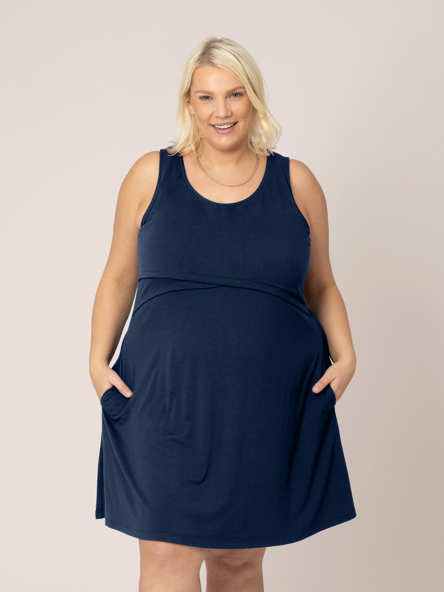 Front view of model wearing the Penelope Crossover Nursing Dress in navy, with hands in pockets. @model_info:Lauren is 5'6" and wearing a 1X.