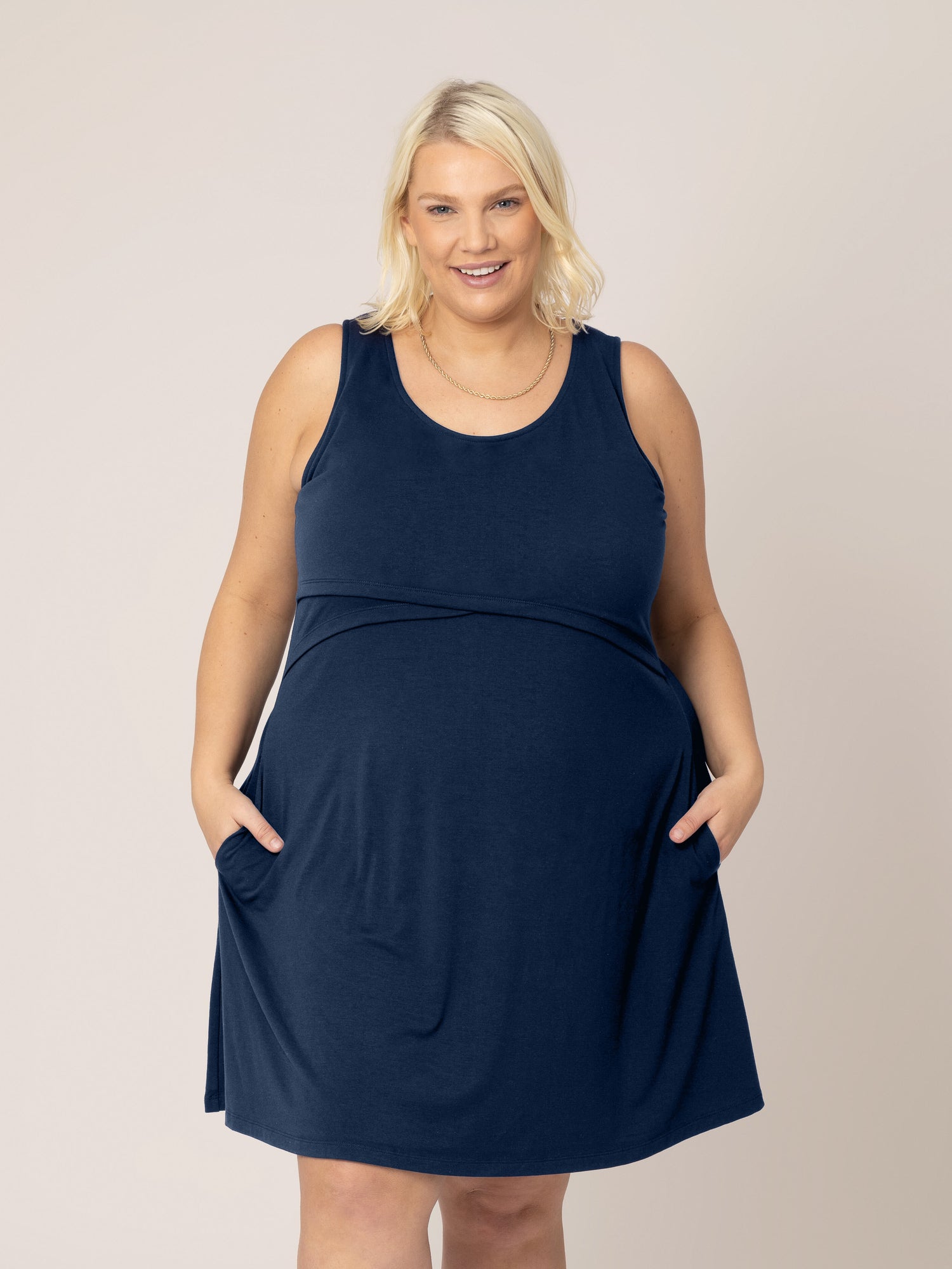 Front view of model wearing the Penelope Crossover Nursing Dress in navy, with hands in pockets. @model_info:Lauren is 5'6" and wearing a 1X.