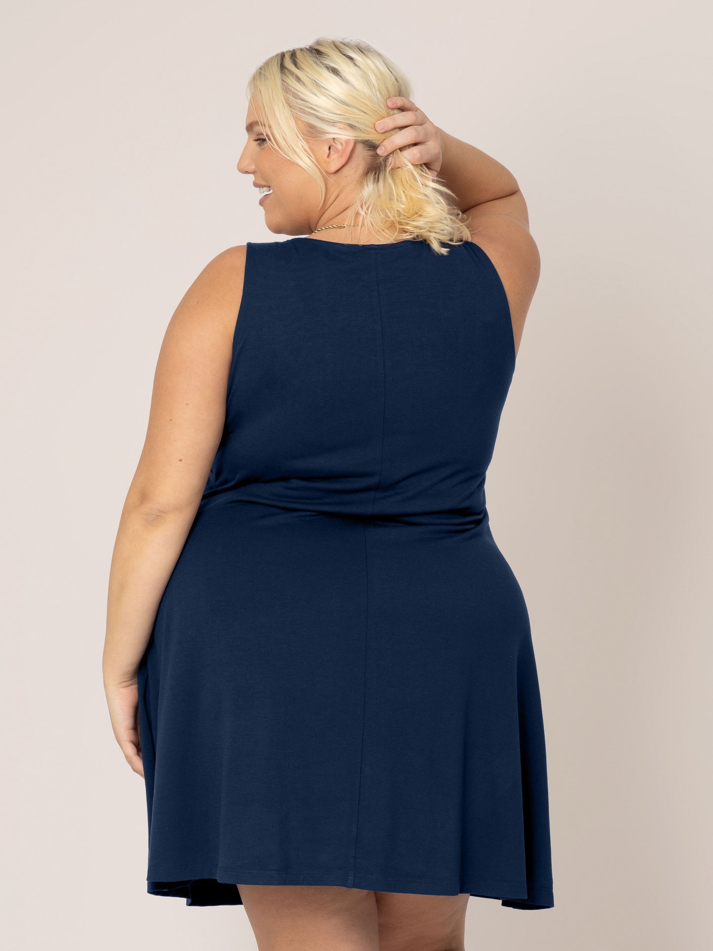 Back view of model pulling hair aside wearing the Penelope Crossover Nursing Dress in navy