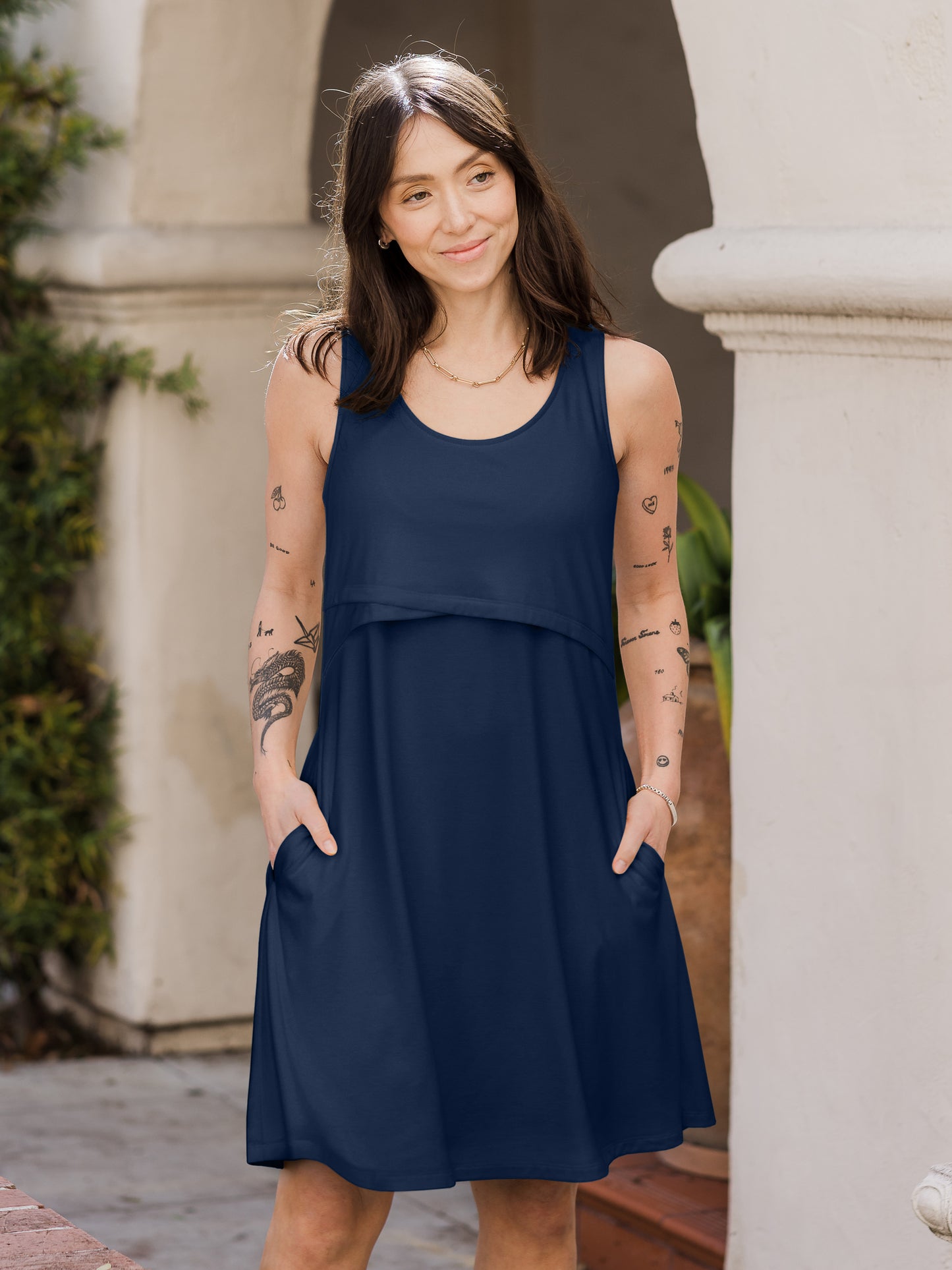 Front view of model outside wearing the Penelope Crossover Nursing Dress in navy, with hands in pockets @model_info:Lyn is wearing a Small.