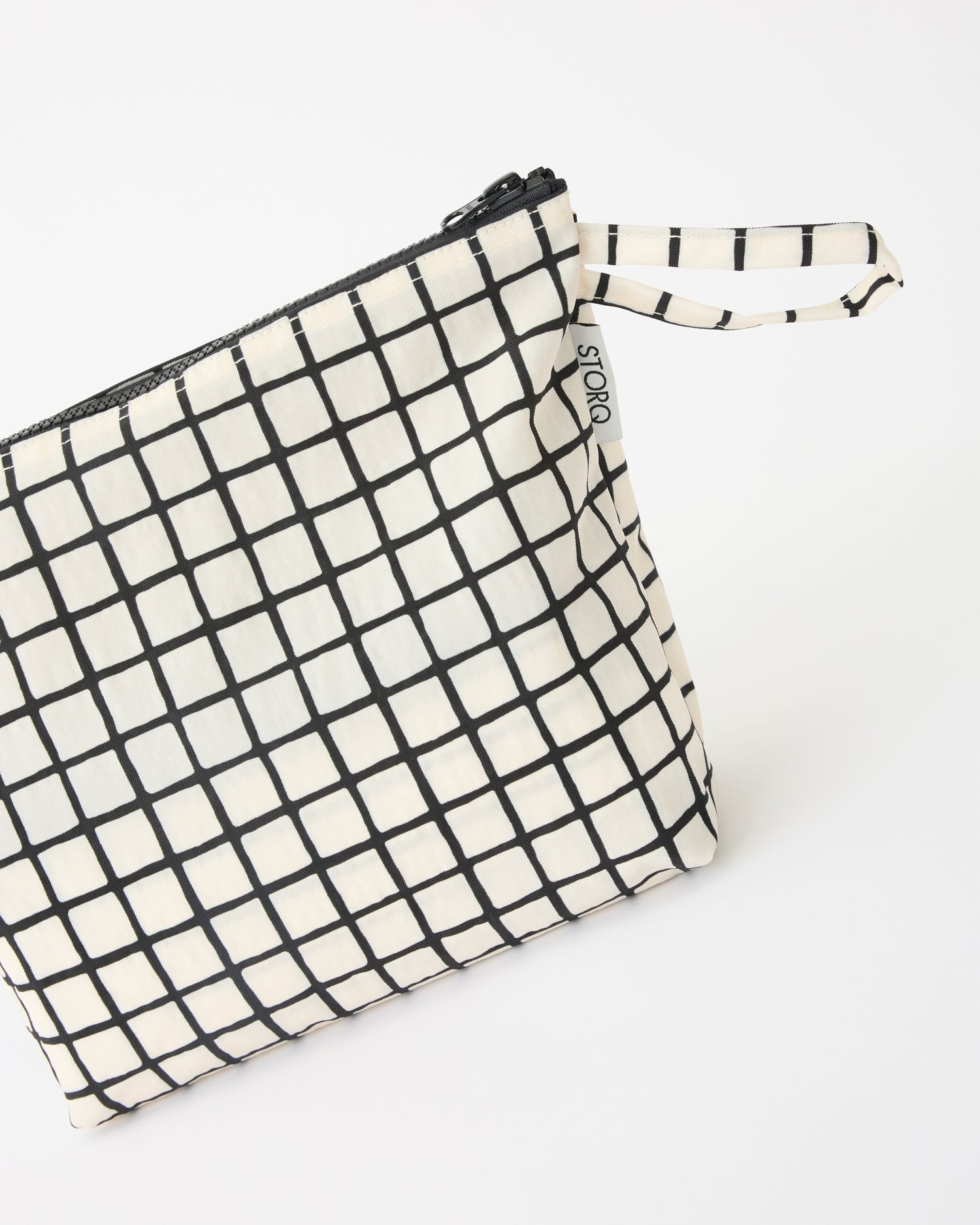 Close up of handle of the Quick Change Kit Bag in Black Grid on a beige background.