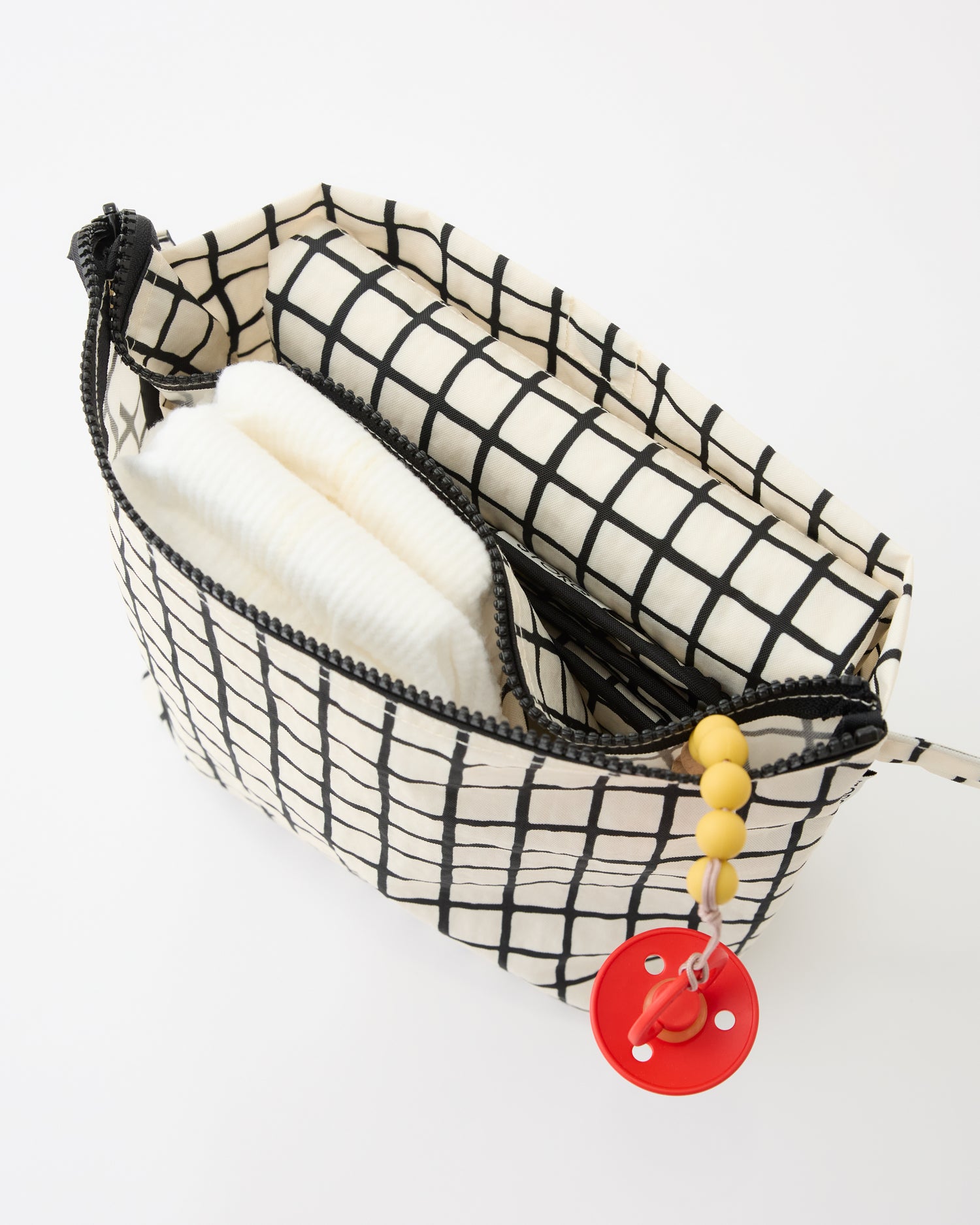 Close up of diaper, pacifier and folded mat inside pocket of the Quick Change Kit Bag in Black Grid, on a beige background.