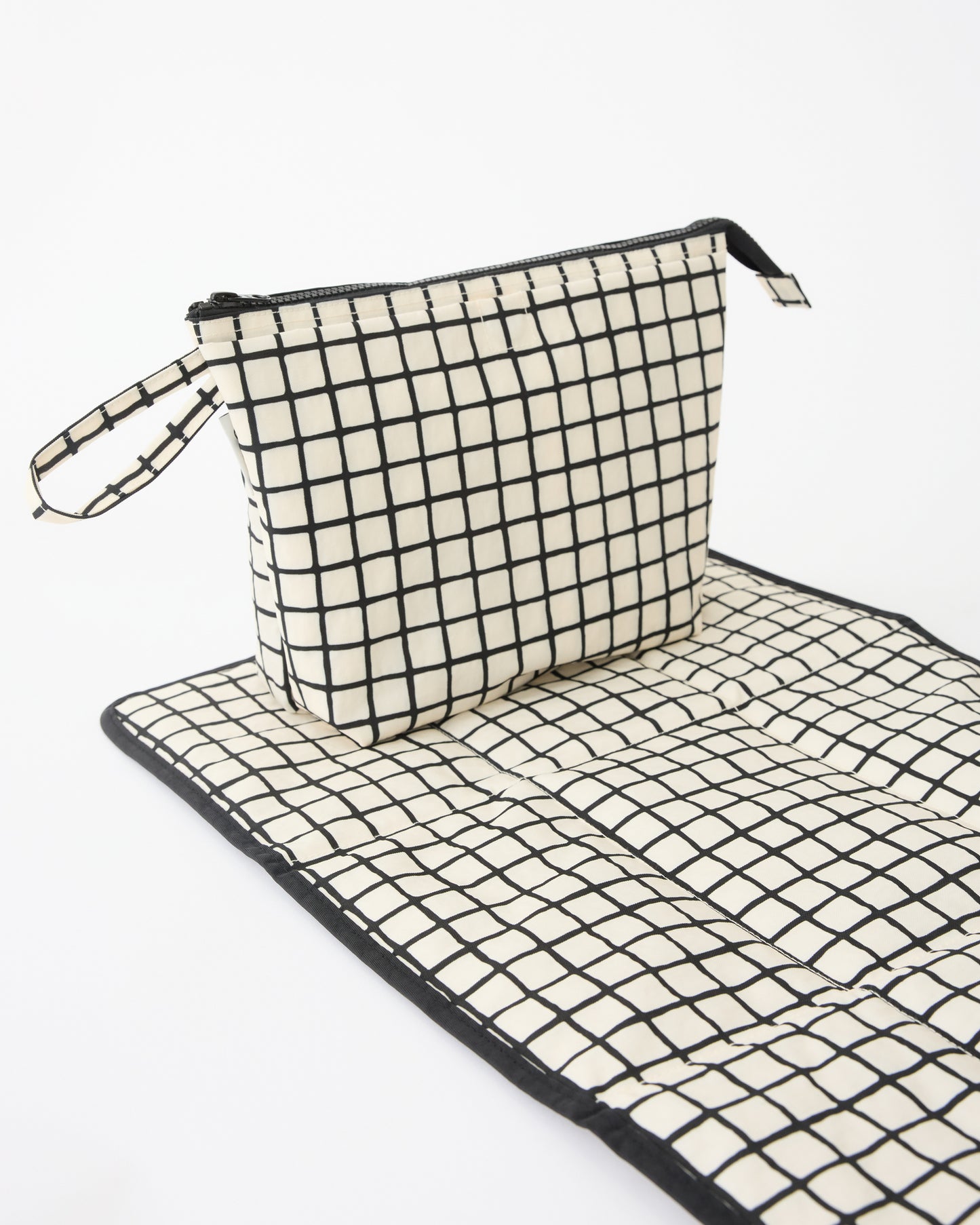 Quick Change Kit Bag in Black Grid, resting on matching changing mat, on a beige background.