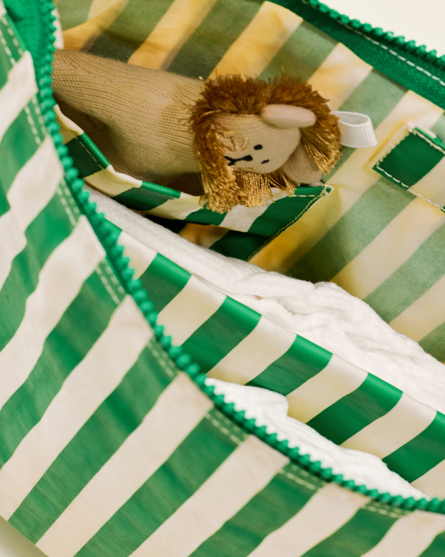 Close up of Quick Change Kit Bag in Green Stripe print, showing the inside with a nappy and a small stuff toy