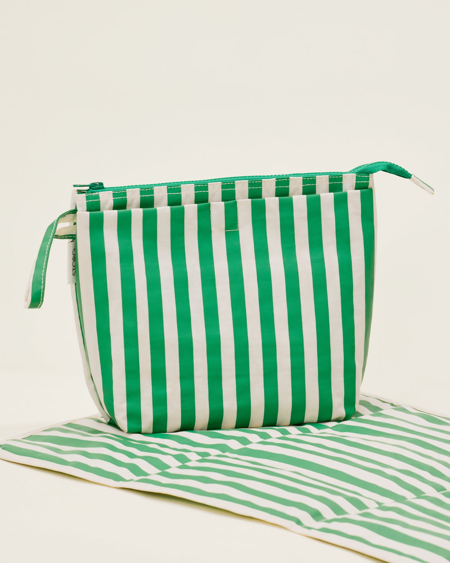 Quick Change Kit Bag in Green Stripe print, on a neutral background, with the included changing pad open under it