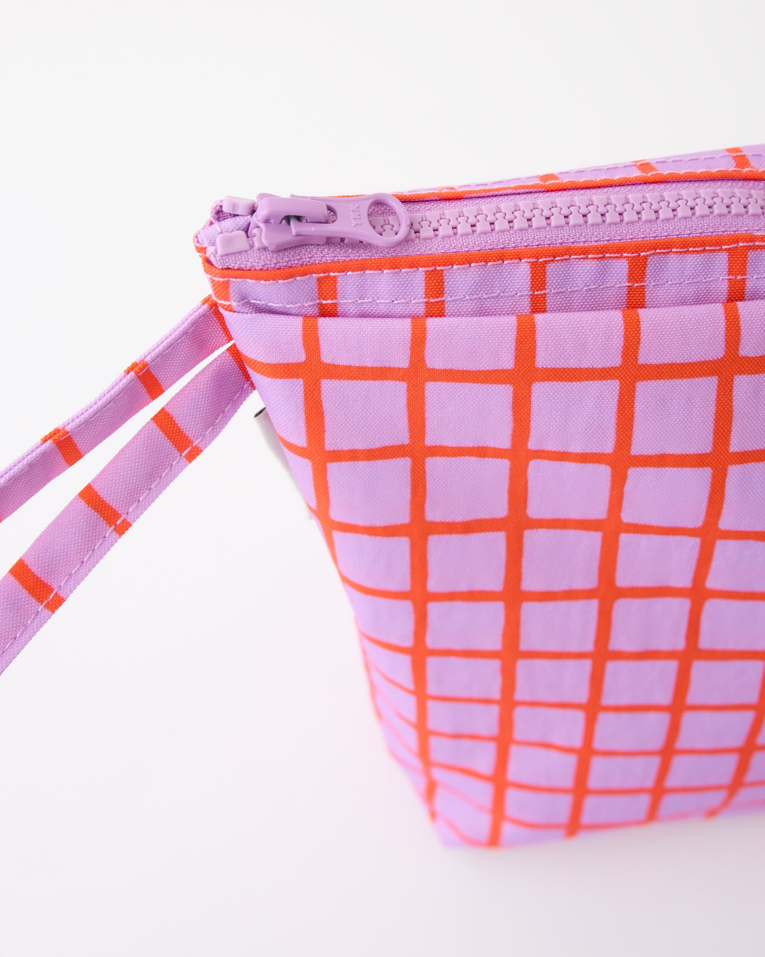 Close up of handle of the Quick Change Kit Bag in Orchid Grid, on a beige background.