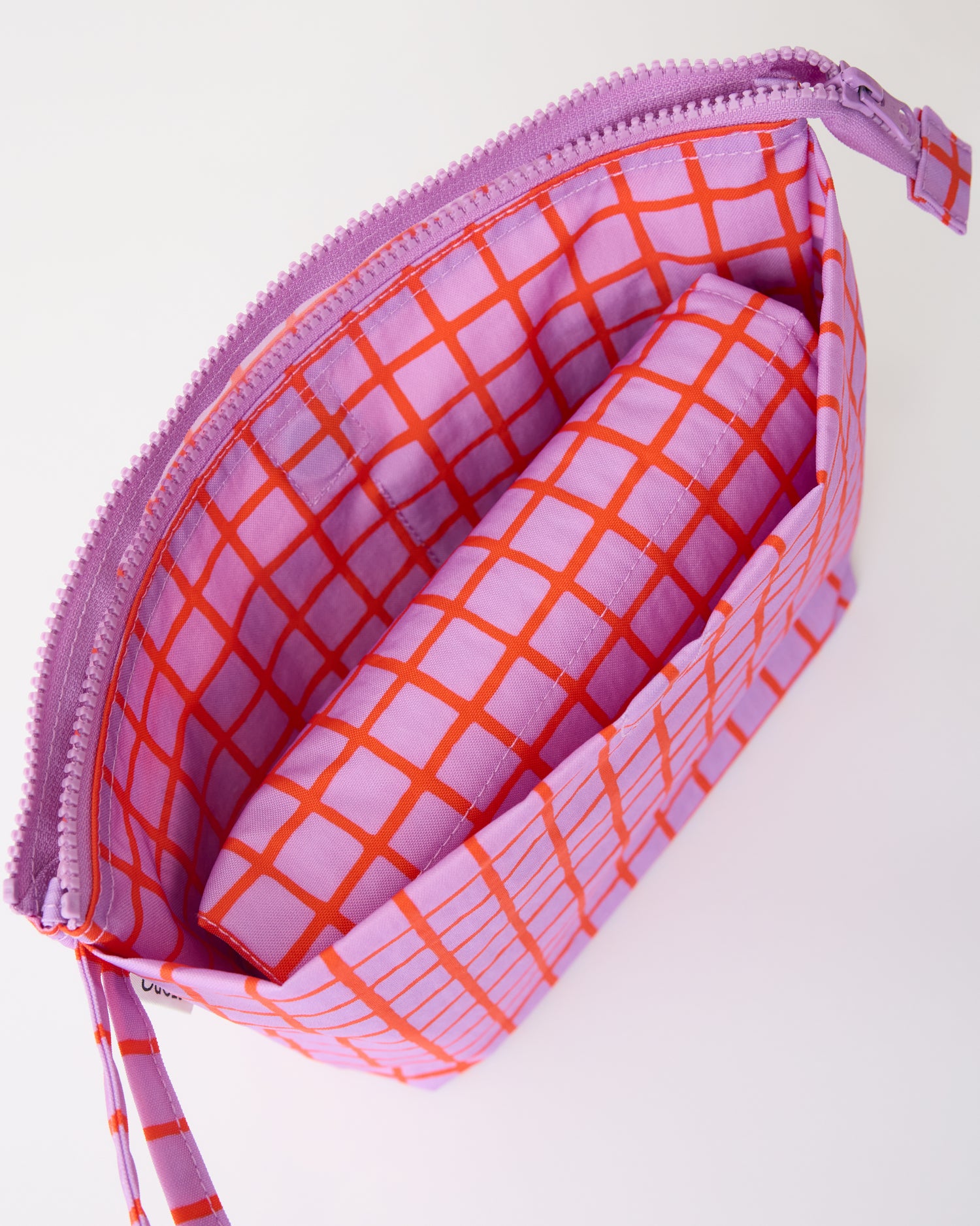 Close up of folded mat inside pocket of the Quick Change Kit Bag in Orchid Grid, on a beige background.