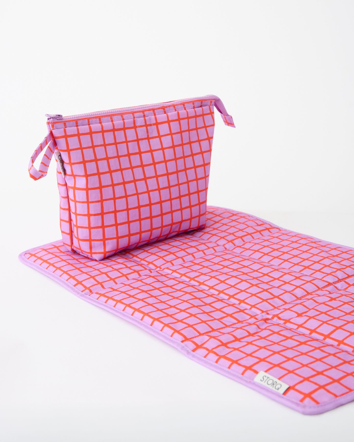 Quick Change Kit Bag in Orchid Grid, resting on matching changing mat, on a beige background.
