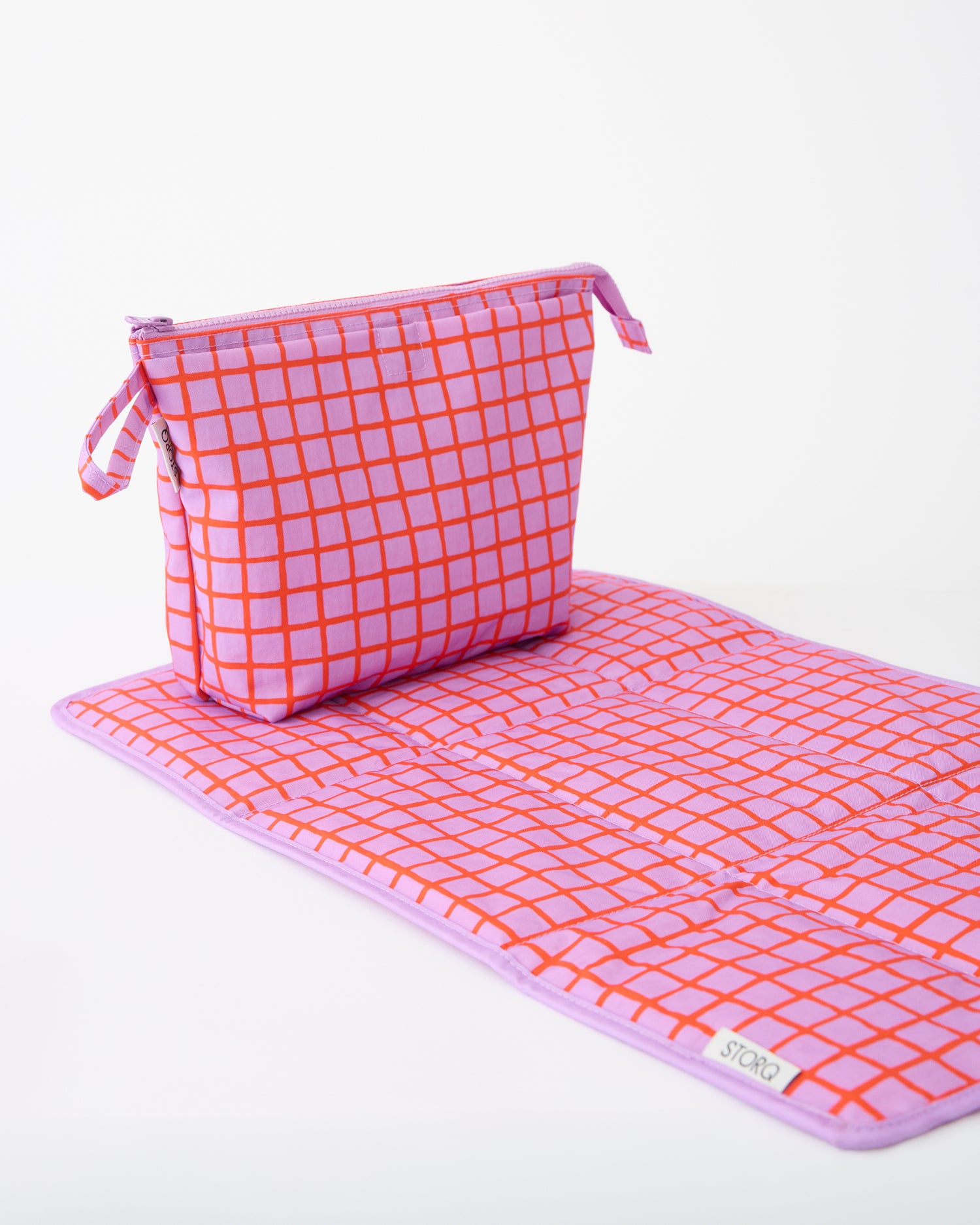Quick Change Kit Bag in Orchid Grid, resting on matching changing mat, on a beige background.