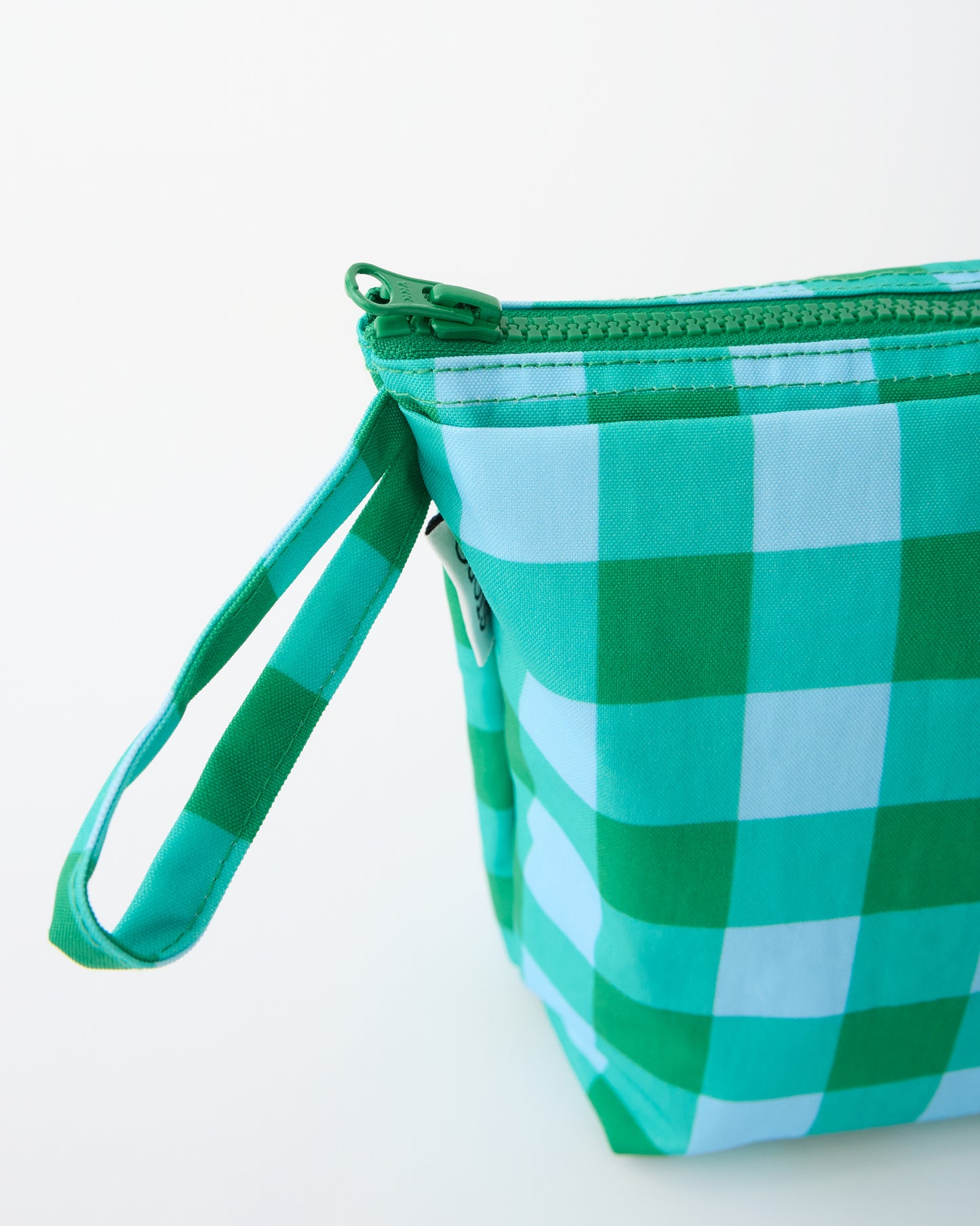 Close up of handle of the Quick Change Kit Bag in Teal Gingham, on a beige background.