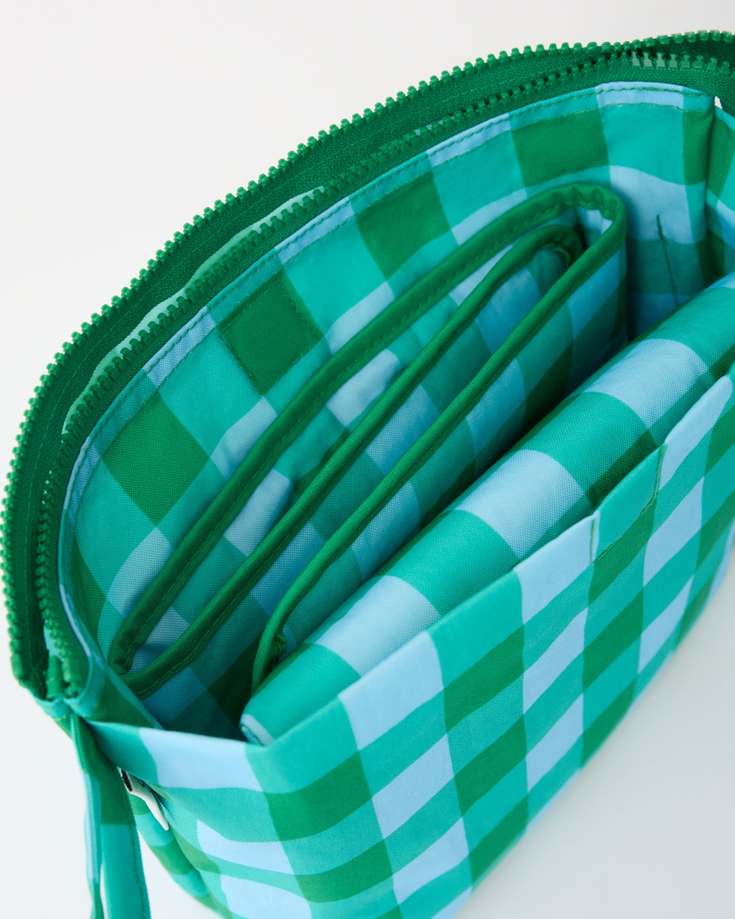 Close up of folded mat inside pocket of the Quick Change Kit Bag in Teal Gingham, on a beige background.