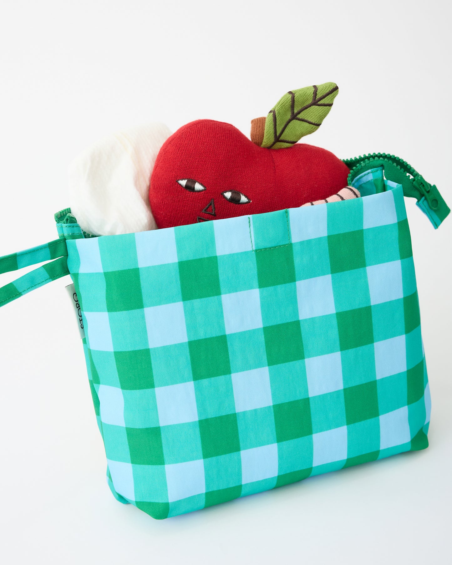 Quick Change Kit Bag in Teal Gingham with diaper and apple lovey sticking out of pocket, on a beige background.