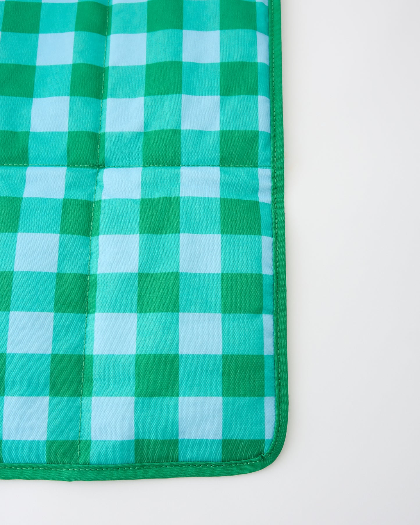 Close up of the folded out mat of the Quick Change Kit Bag in Teal Gingham, on a beige background.