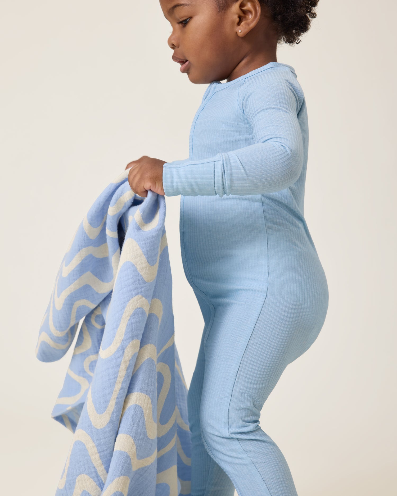 Baby holding a blue muslin pattern fabric and wearing the Ribbed Bamboo Baby Pajama in Blue Heather