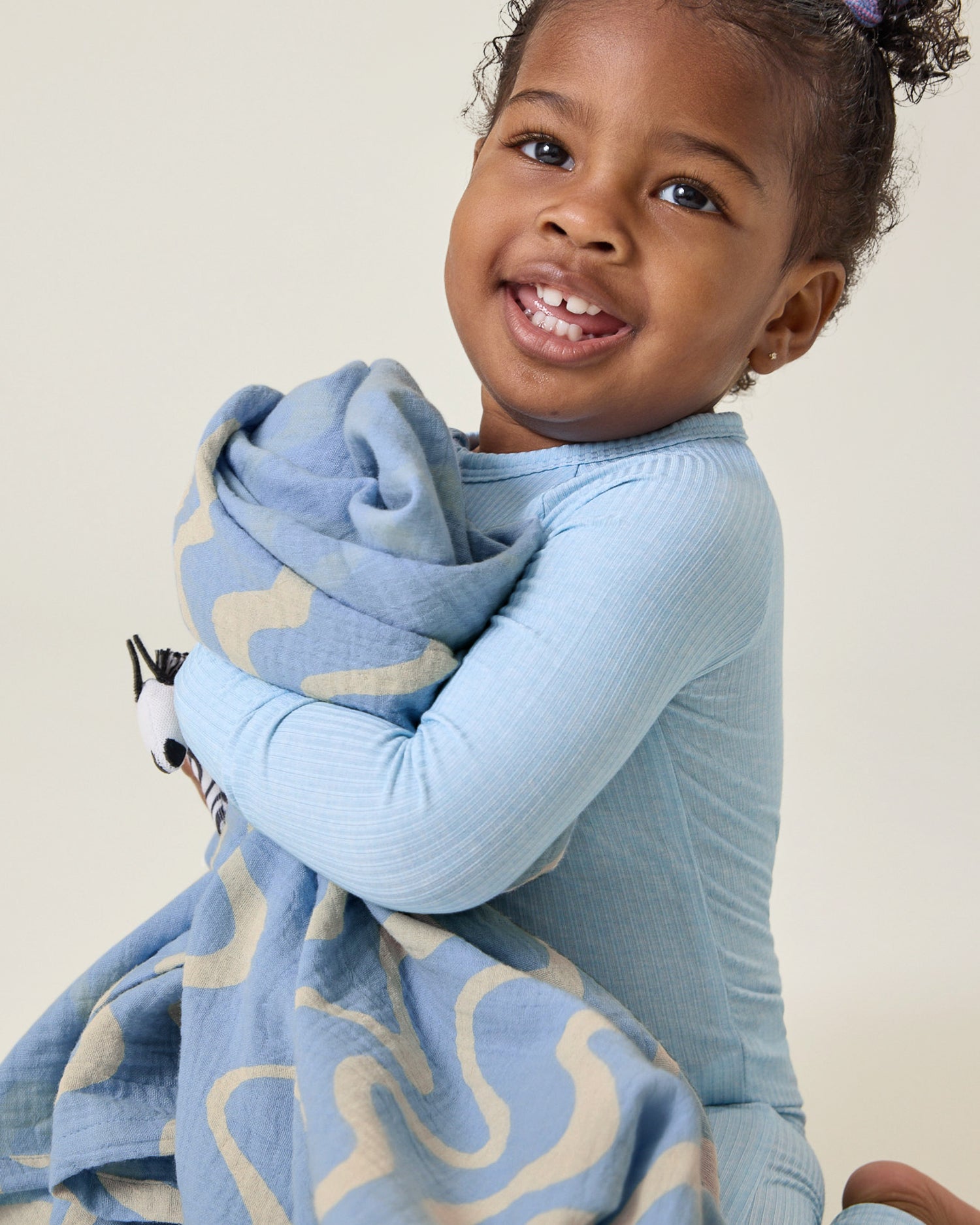 Child holding the Organic Muslin Swaddle in the Blue Waves print.