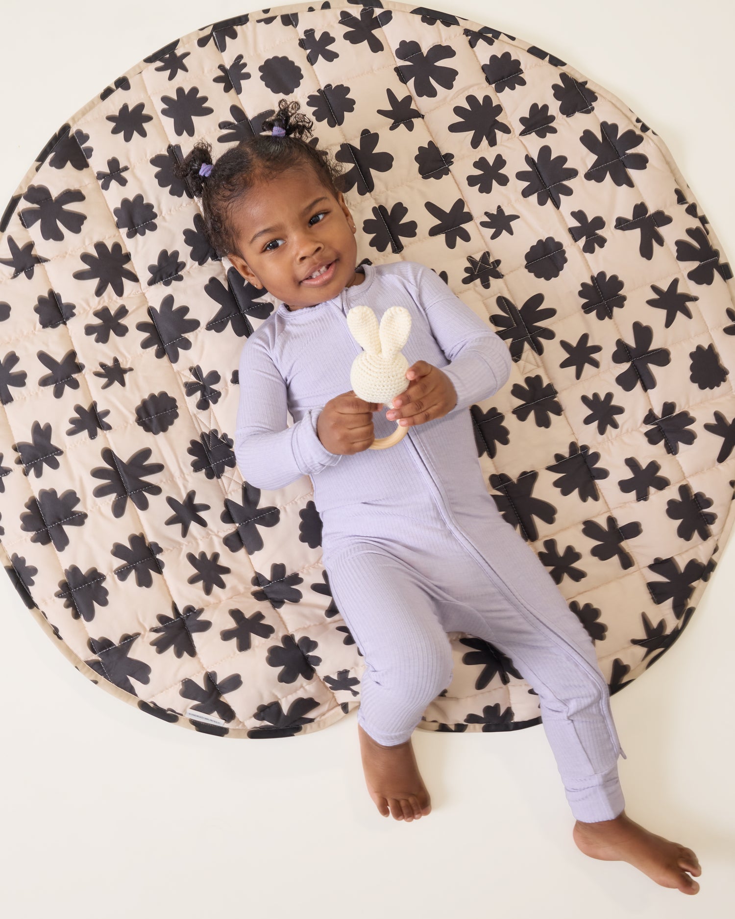 Baby lying down on a black and white patterned mat, wearing the Ribbed Bamboo Baby Pajama in Lilac Heather