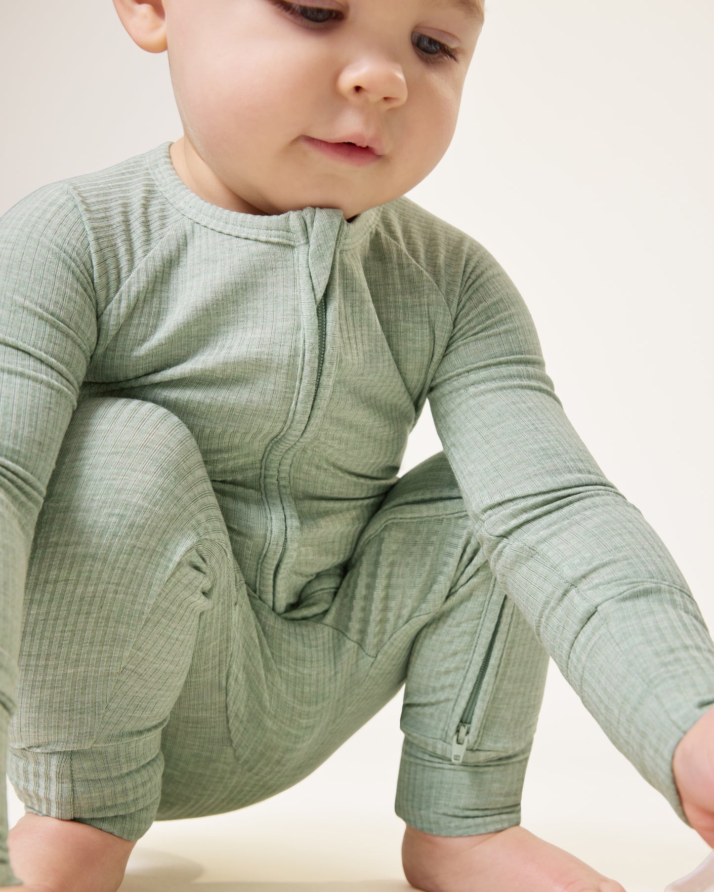 Baby squatting and looking down, wearing the Ribbed Bamboo Baby Pajama in Sage Heather