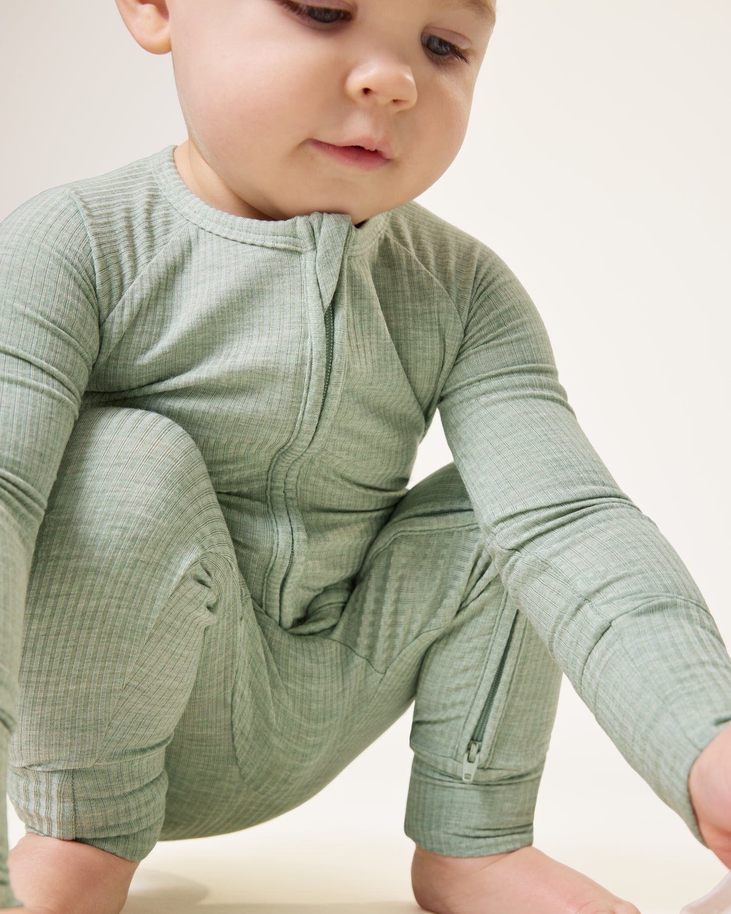 Baby squatting and looking down, wearing the Ribbed Bamboo Baby Pajama in Sage Heather