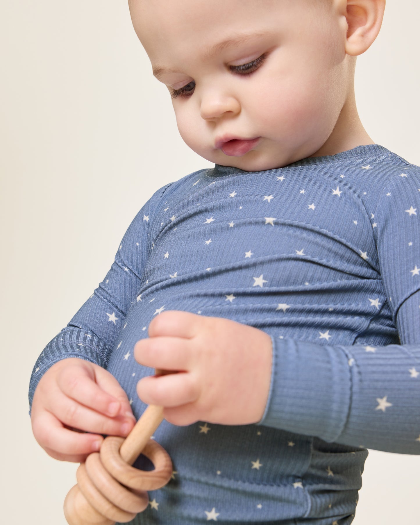 Baby looking down, holding a wooden toy, wearing the Ribbed Bamboo Baby Two-Piece Pajama Set in Blue Stars