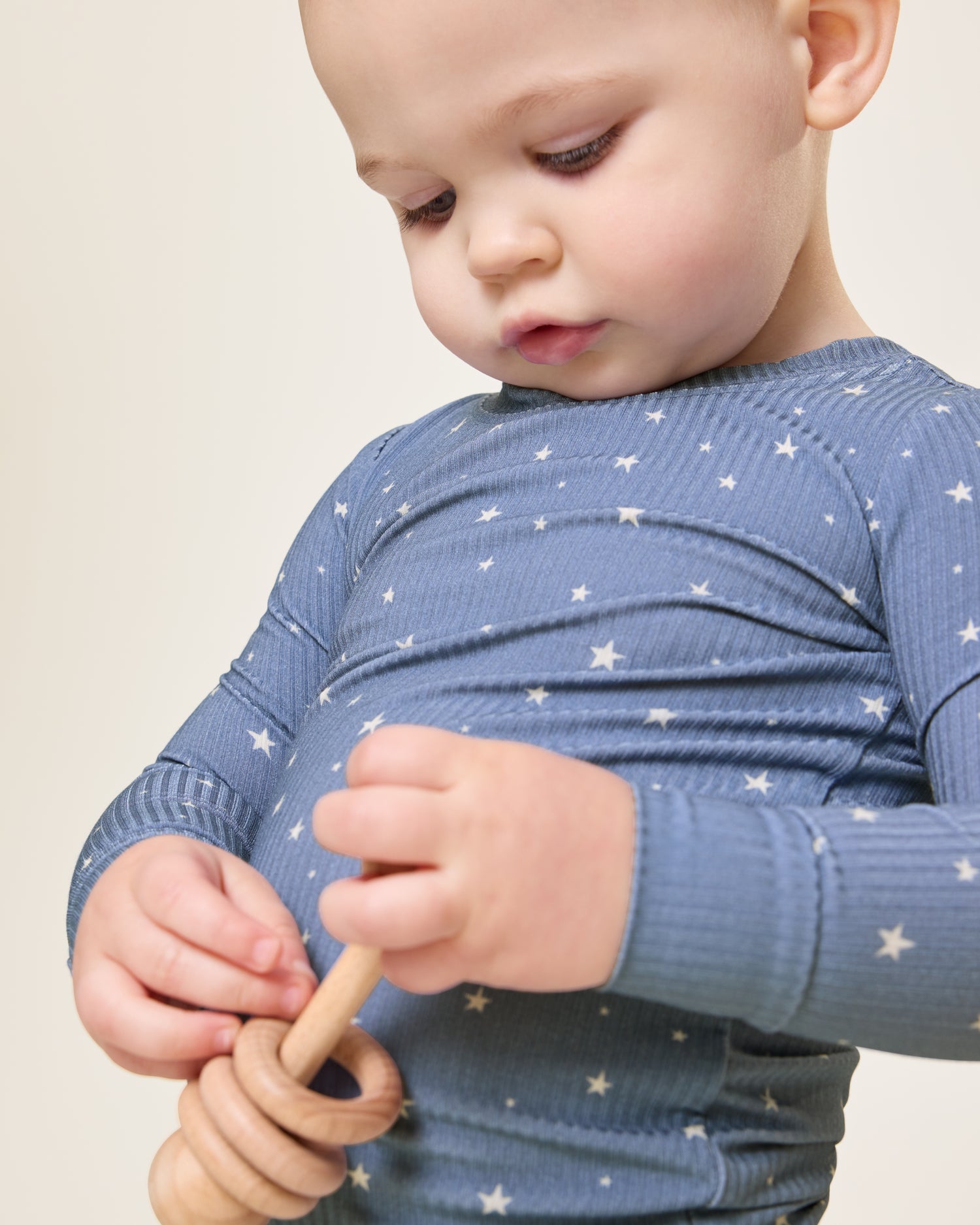 Baby looking down, holding a wooden toy, wearing the Ribbed Bamboo Baby Two-Piece Pajama Set in Blue Stars