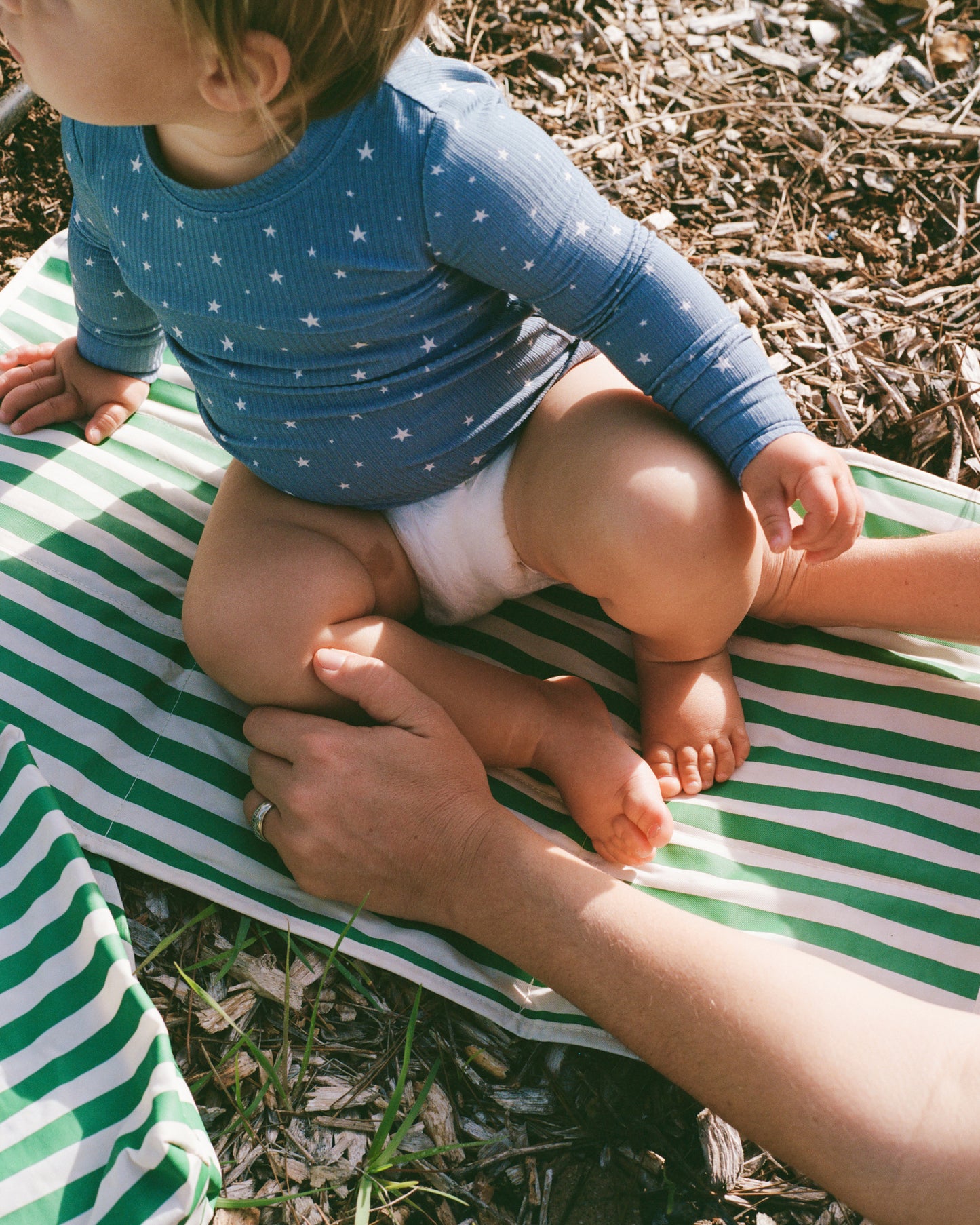Baby sitting on Quick Change Kit Bag in Green Stripe outside