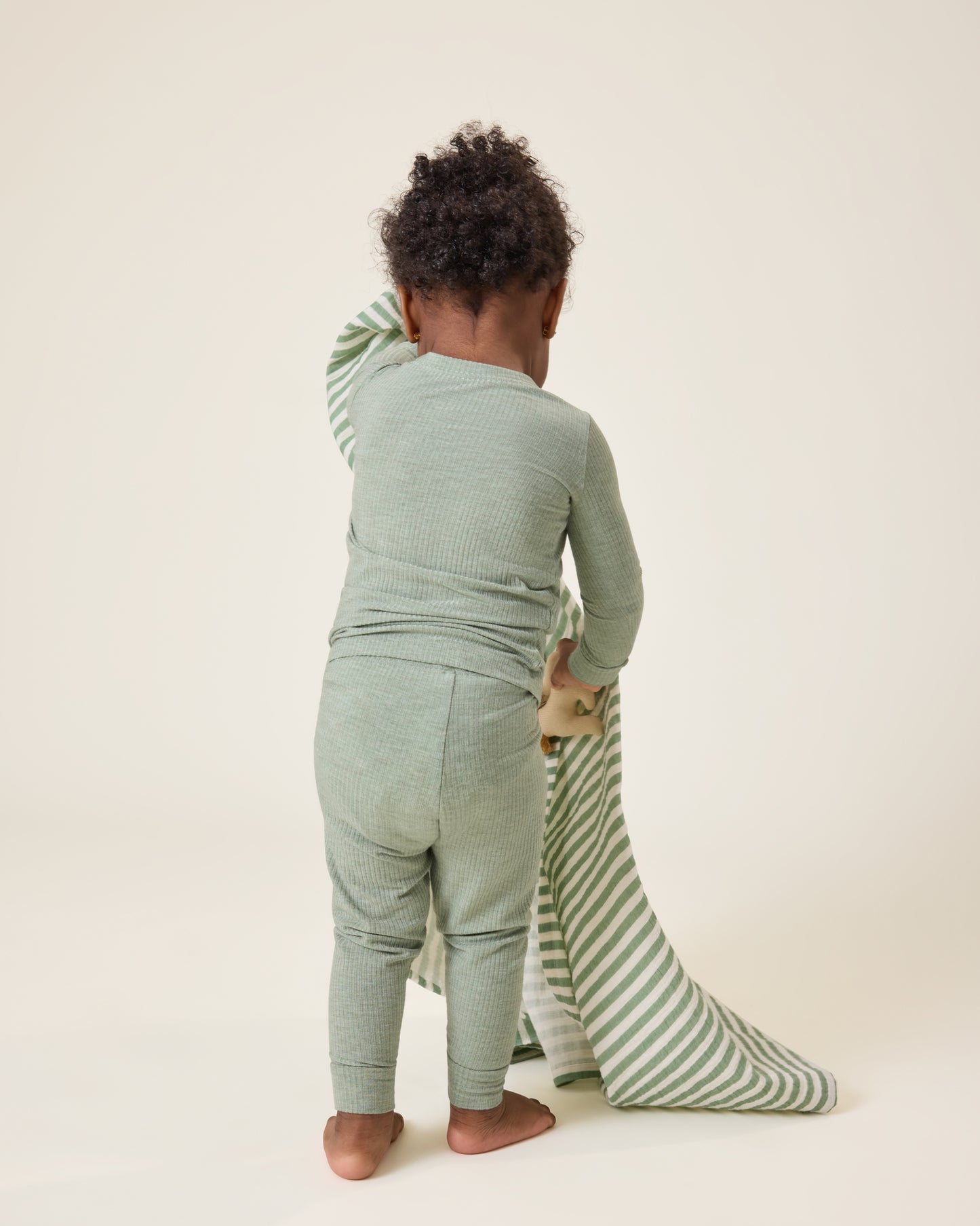 Baby holding a patterned blanket, wearing the Ribbed Bamboo Baby Two-Piece Pajama Set in Sage Heather