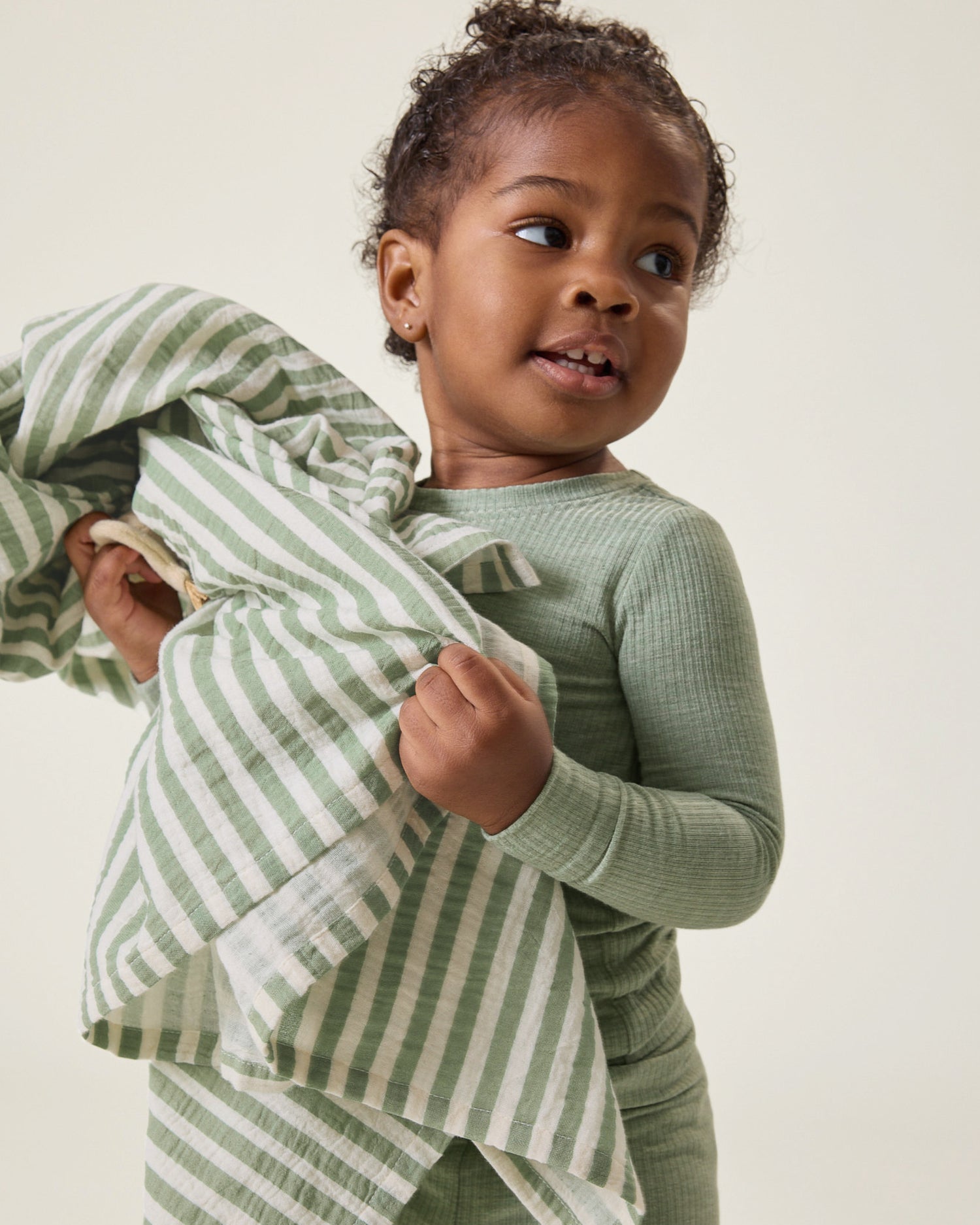 Child holding the Organic Muslin Swaddle in the Sage Stripe print against a neutral background