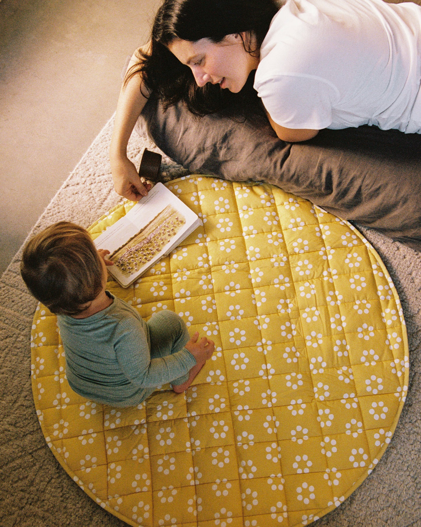 Child sitting on the Inside/Outside Play Mat in Sunshine Dots print with adult looking at a book